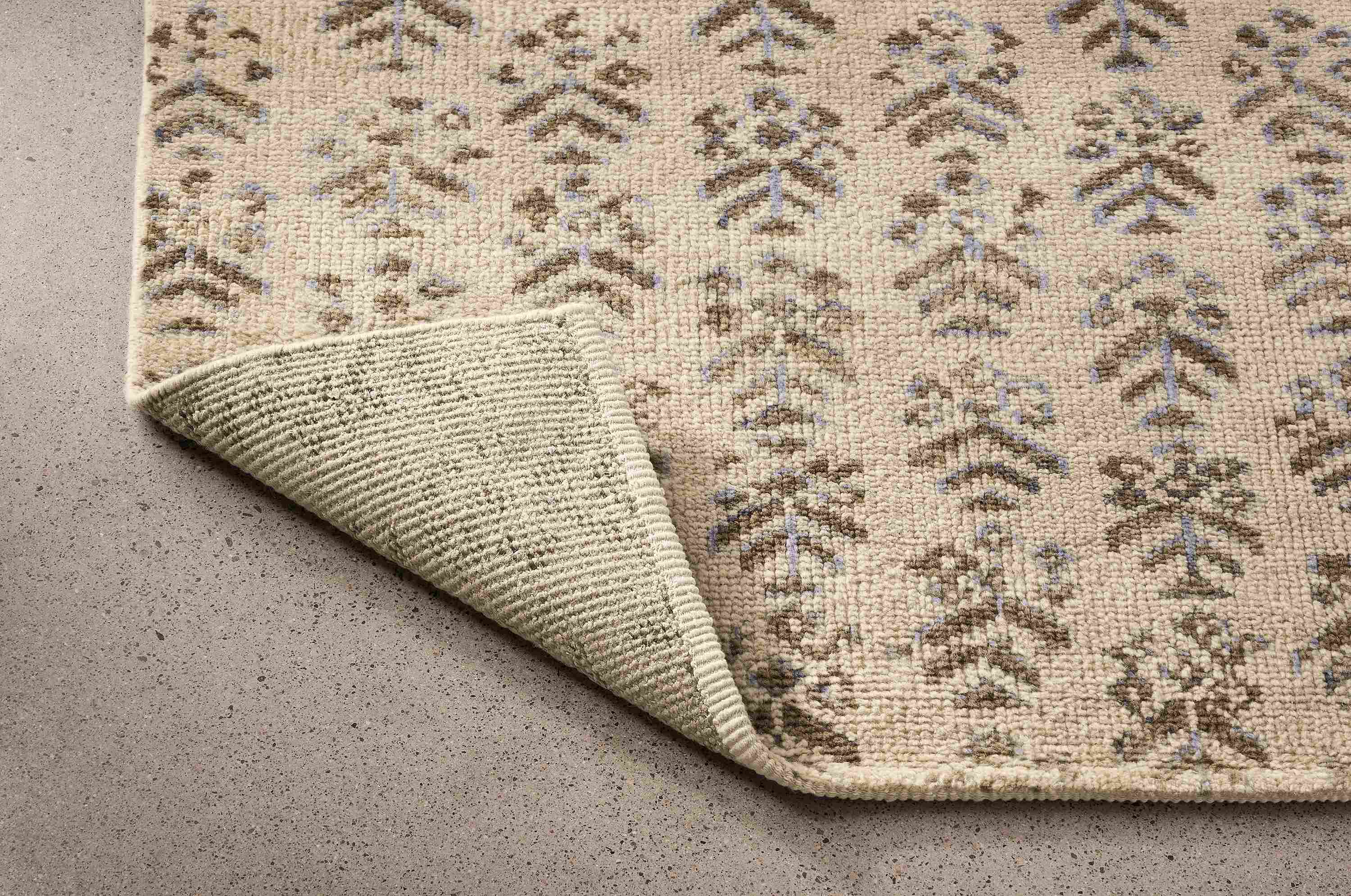 Detail of Leyla 8 by 10 rug in snow shown with corner flipped up to show underside of rug.