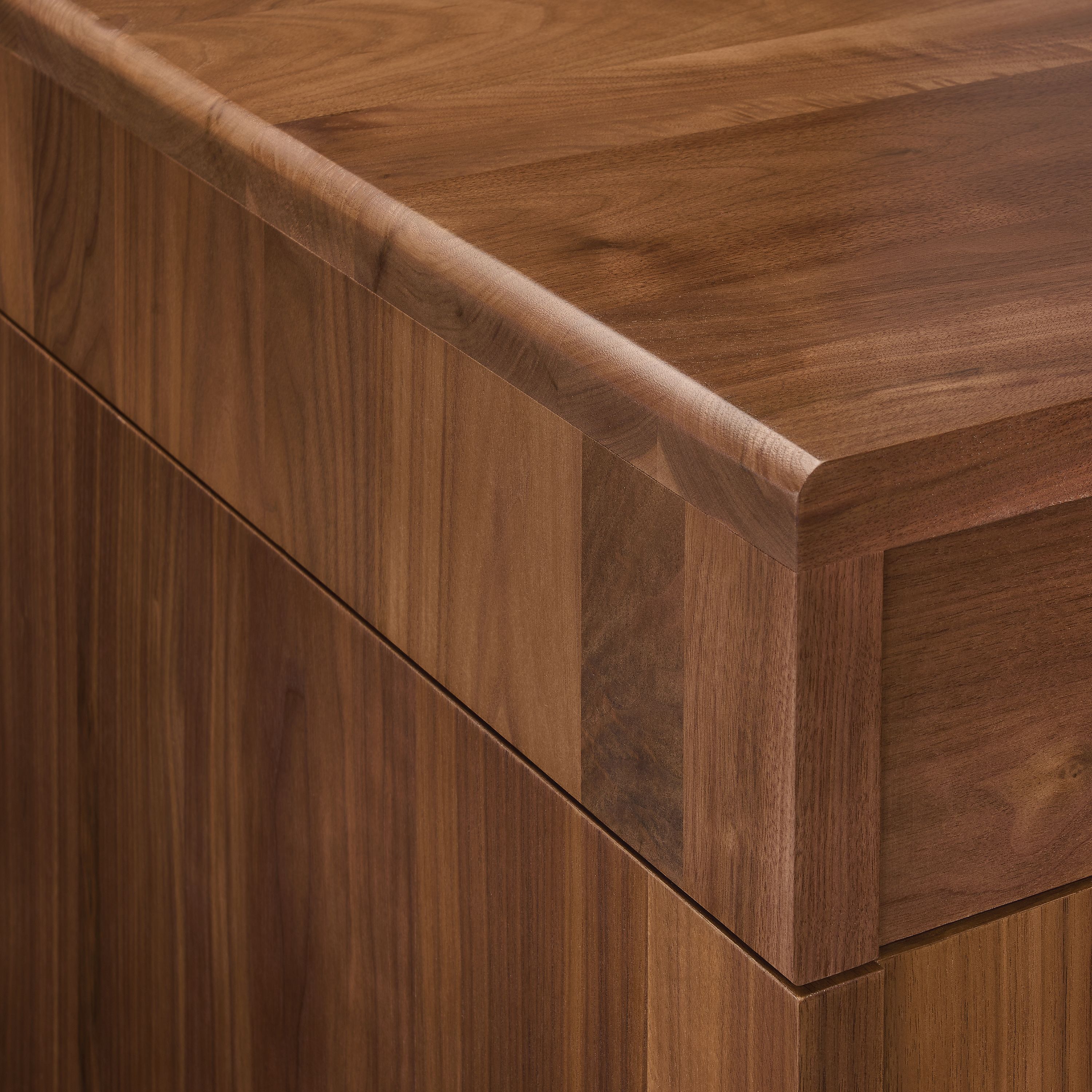 Detail of Lincoln adjustable standing desk in walnut showing corner of desk and seam where top and base meet.