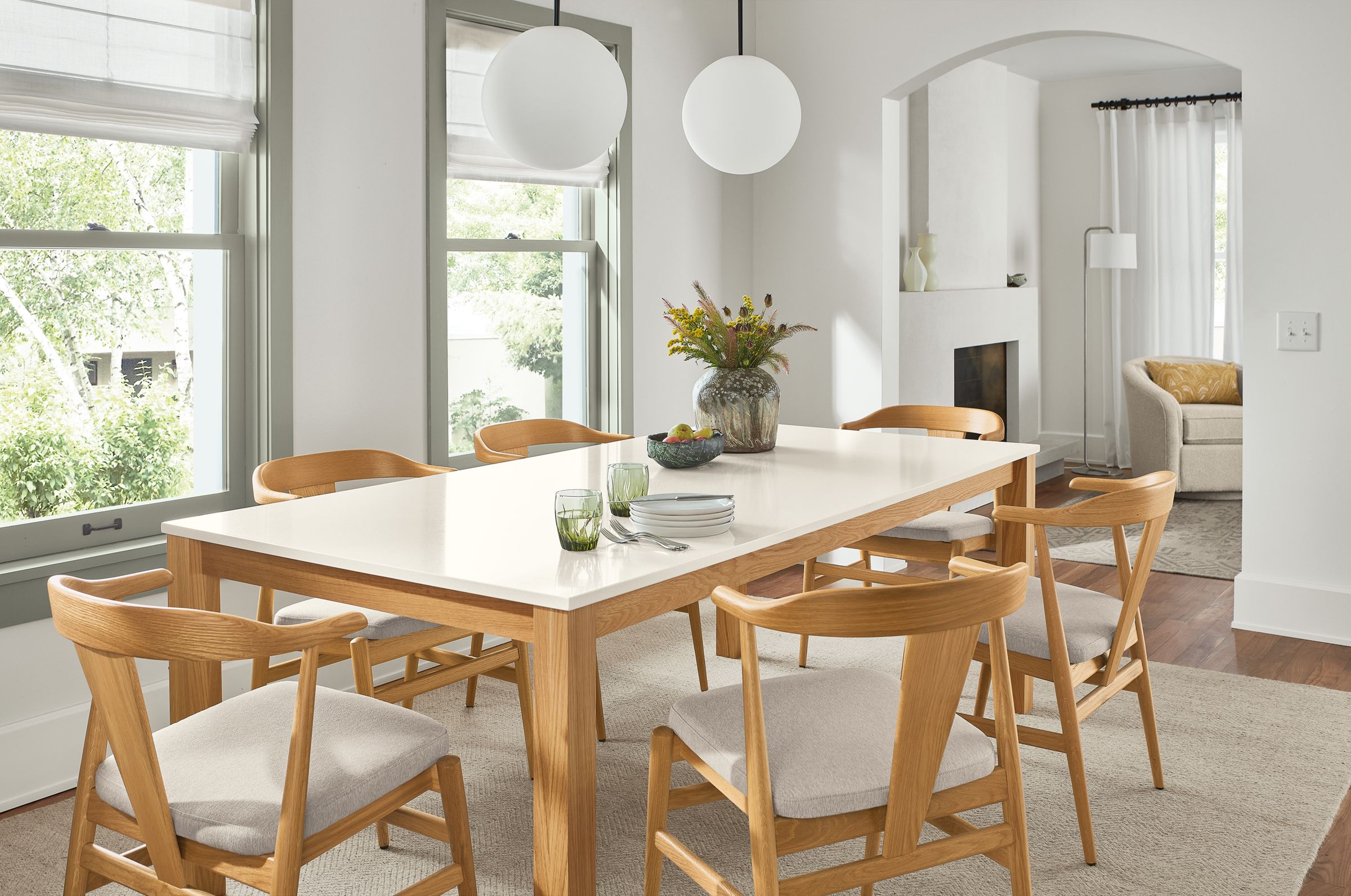 dining room with linden table with white quartz top and white oak base, 6 evan chairs in white oak, two orbit pendants.
