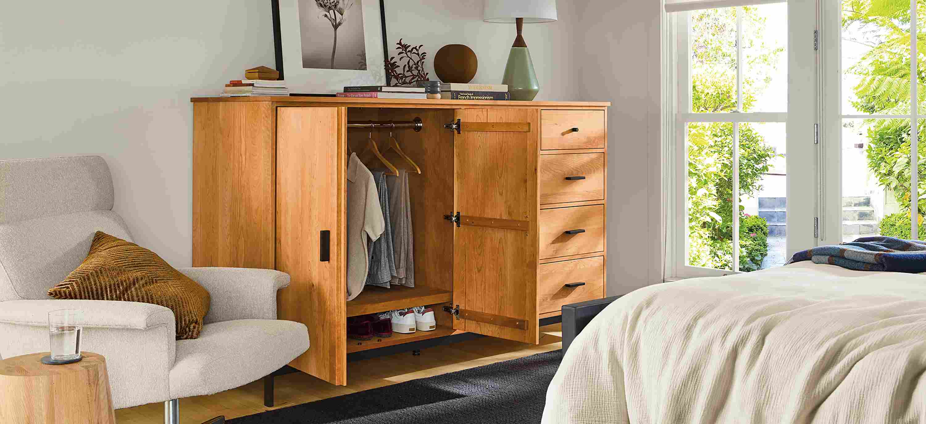 Bedroom with linear 78-wide armoire shown with doors open, Parsons queen standard bed and Nyla table in natural solid red oak.