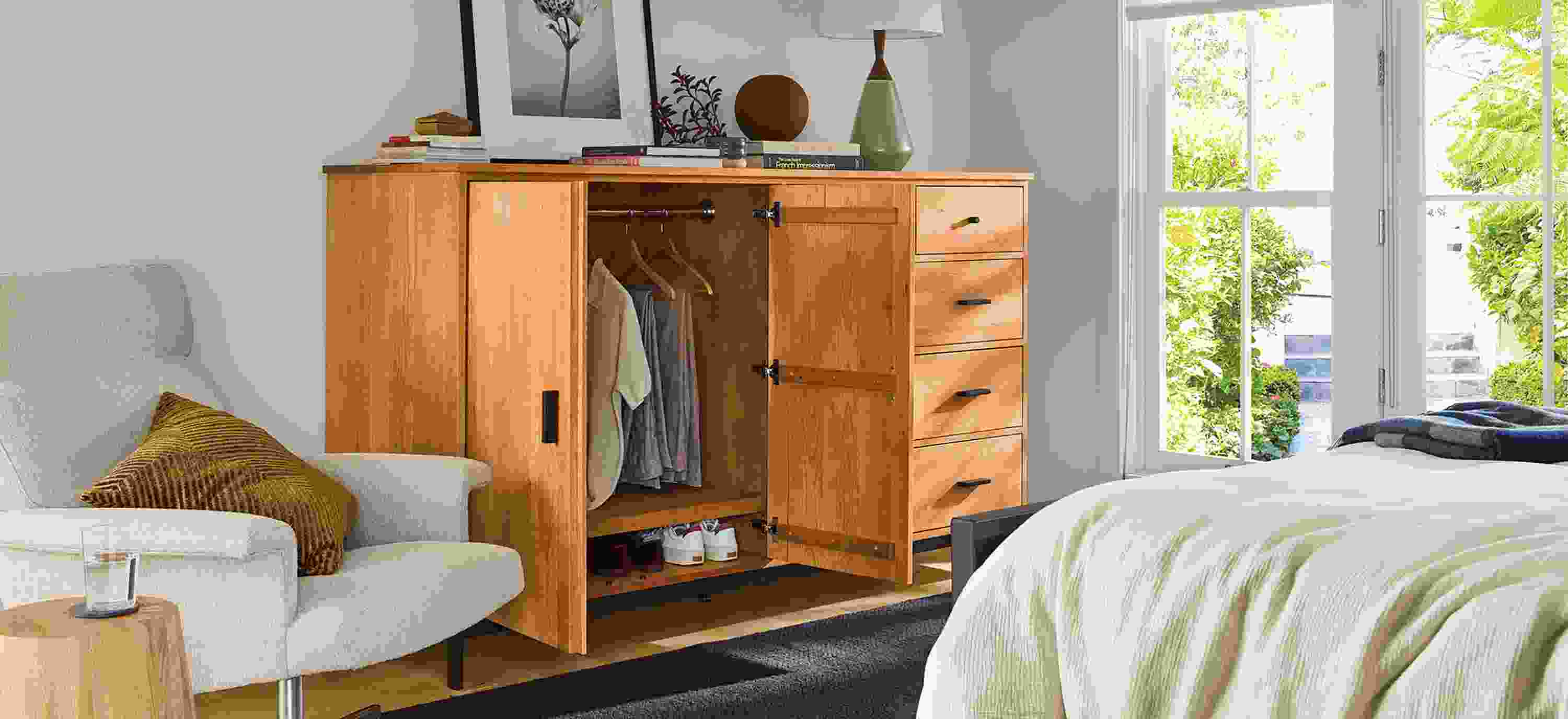 Bedroom with linear 78-wide armoire shown with doors open, Parsons queen standard bed and Nyla table in natural solid red oak.
