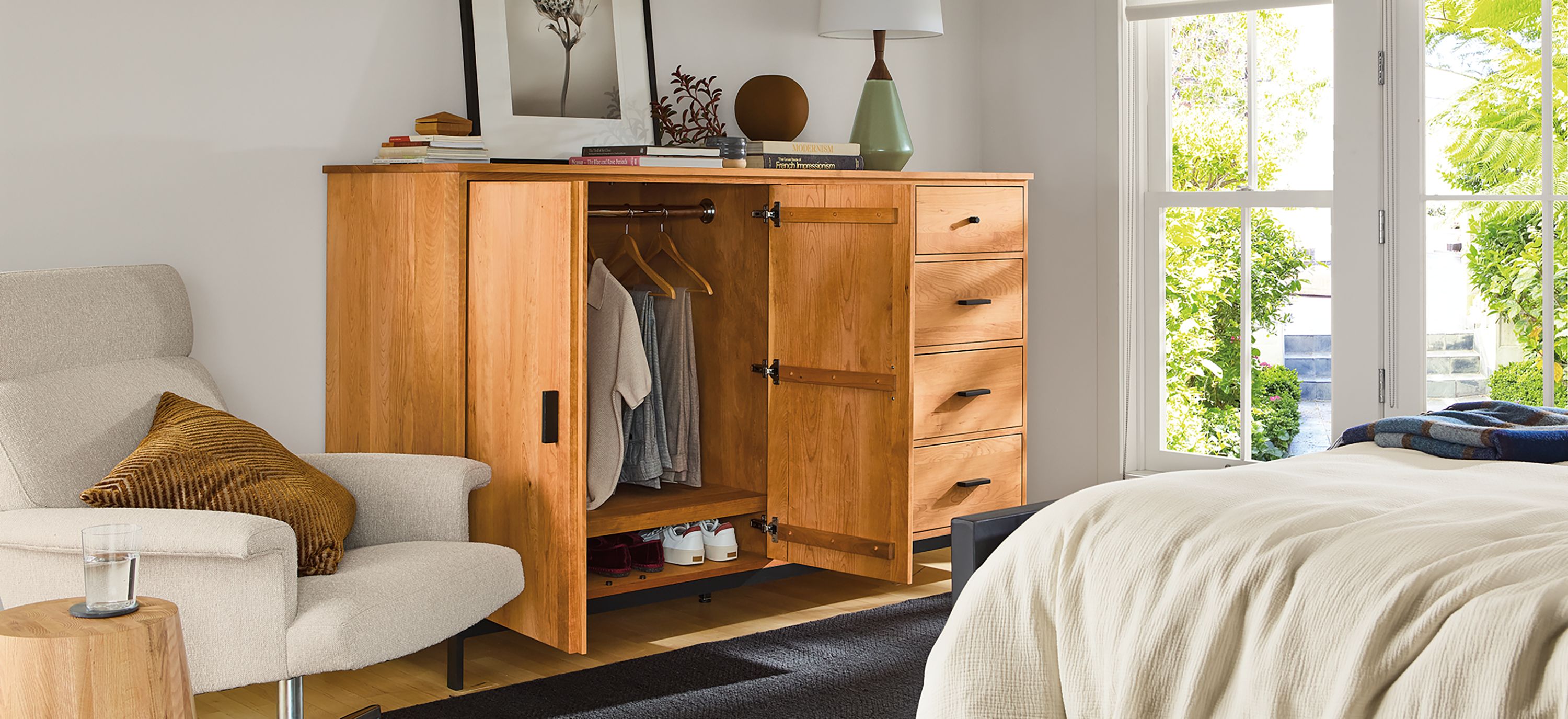 Bedroom with linear 78-wide armoire shown with doors open, Parsons queen standard bed and Nyla table in natural solid red oak.