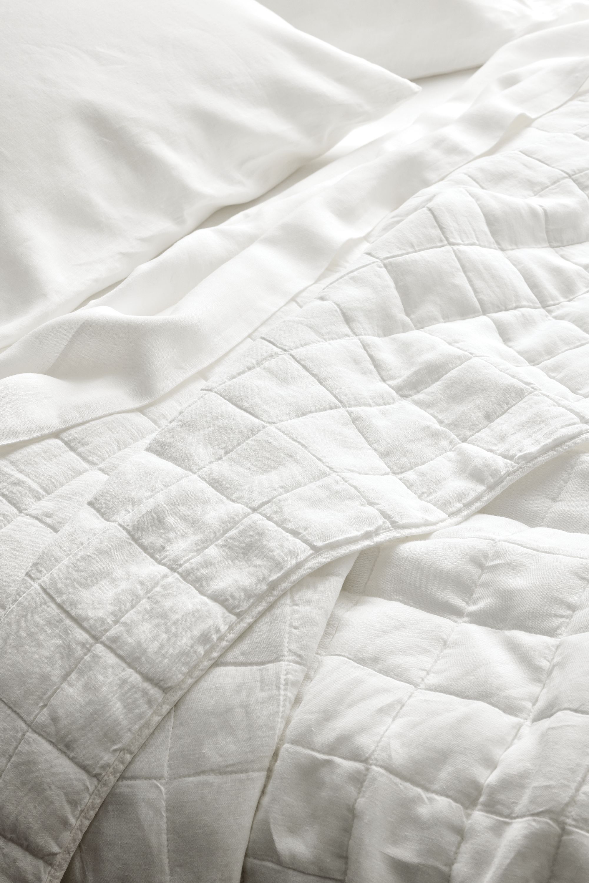 Close-up of relaxed linen full/queen quilted coverlet and relaxed linen queen sheet set in white.