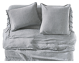 detail of relaxed linen sheet set, shams, duvet cover in blue chambray on bed.