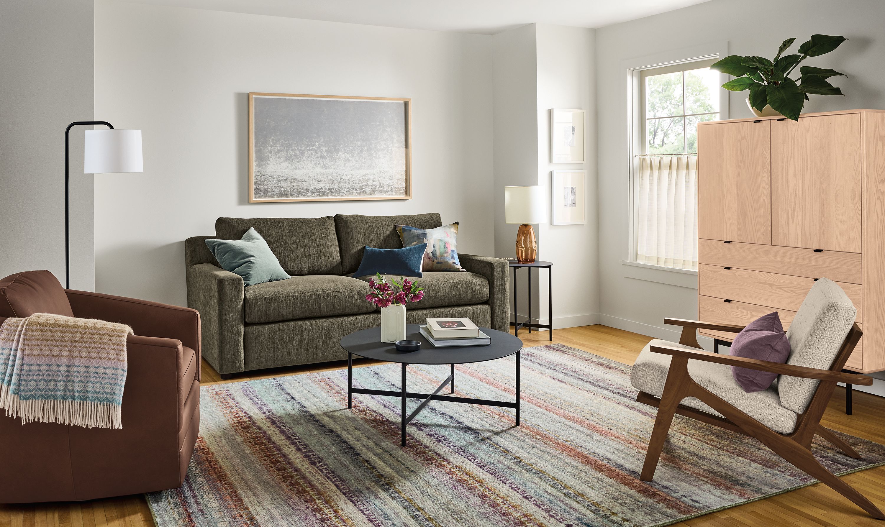 Living room with Ludlow pull-out sleeper sofa in crawford olive, Ford swivel chair in Laino Cognac leather and Varun rug in multicolor.
