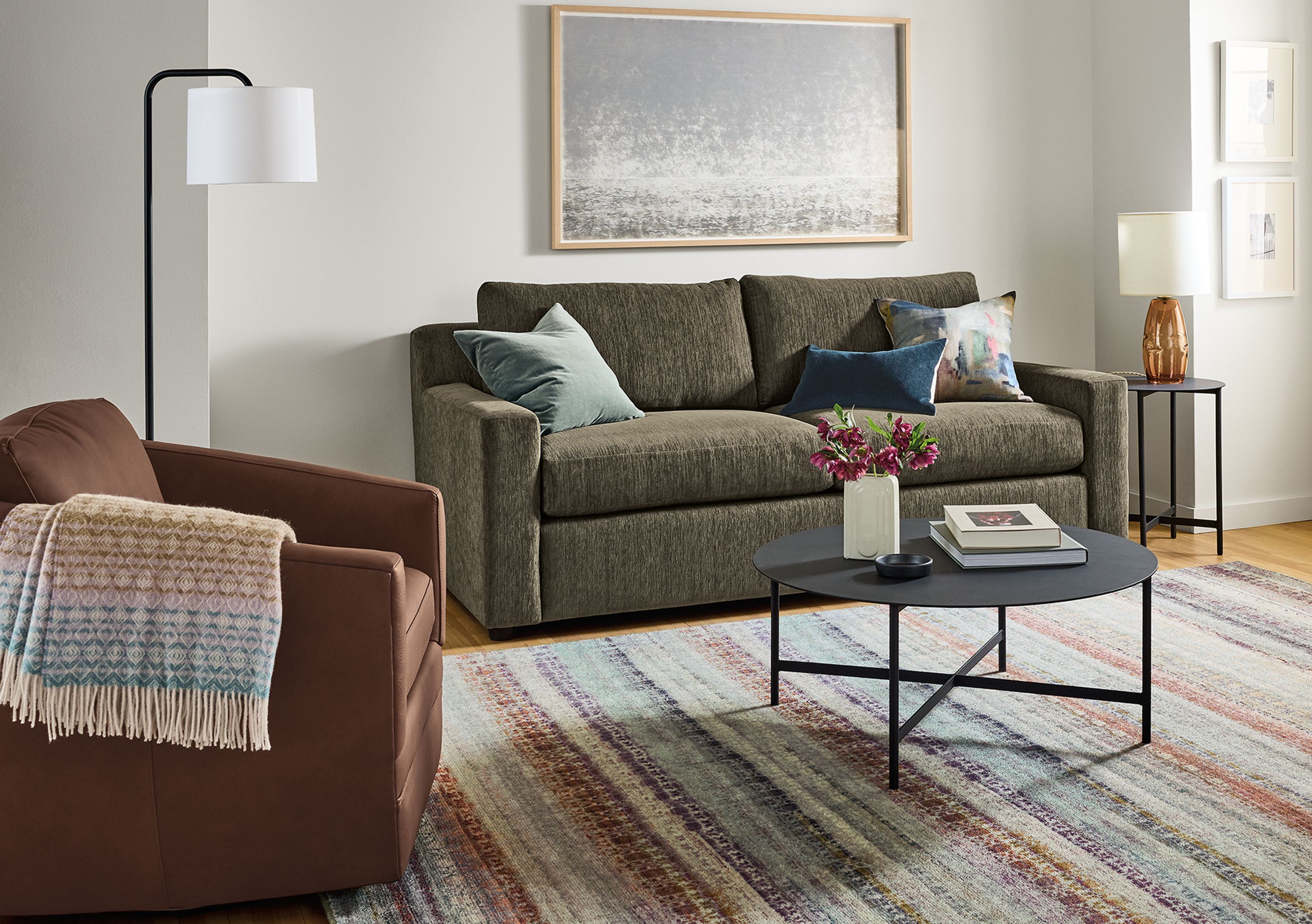 Living room with Ludlow pull-out sleeper sofa in crawford olive, Ford swivel chair in Laino Cognac leather and Varun rug in multicolor.