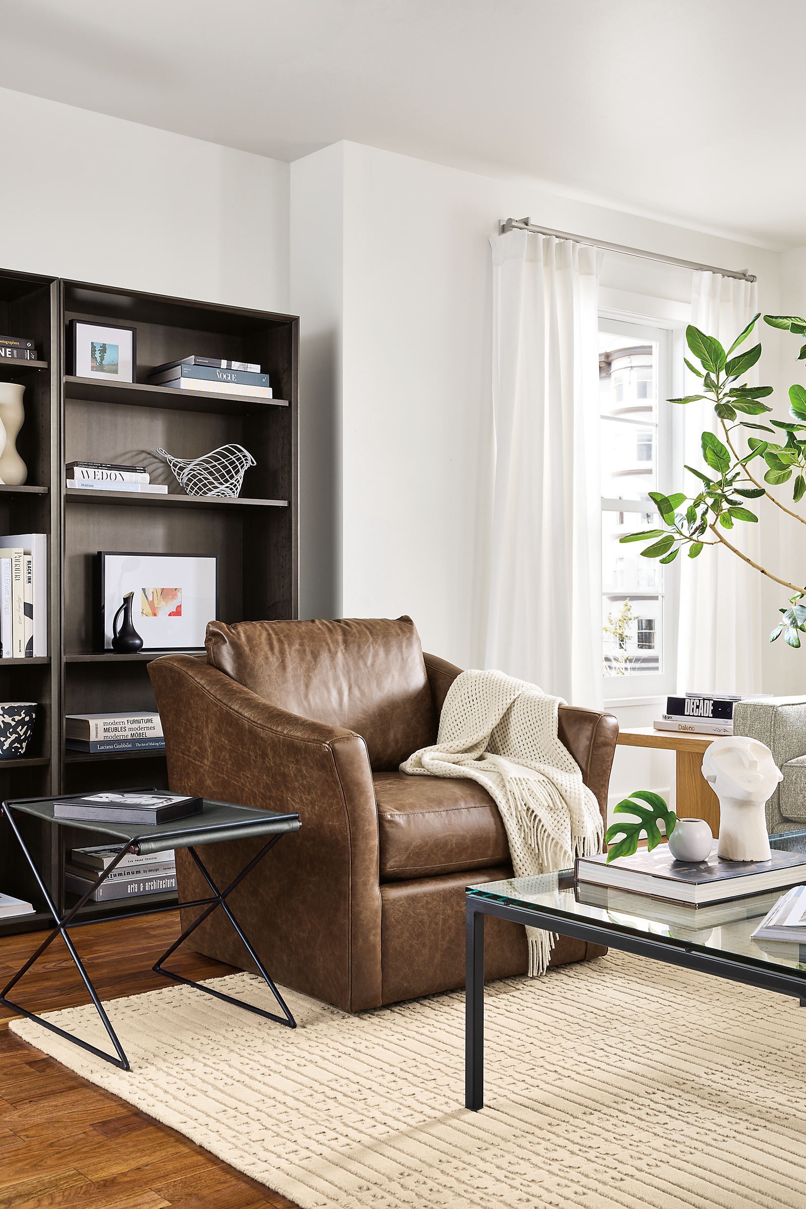 Living room with Maeve swivel chair in bourbon leather, tavi stool in black leather and rollins bookcases in charcoal.