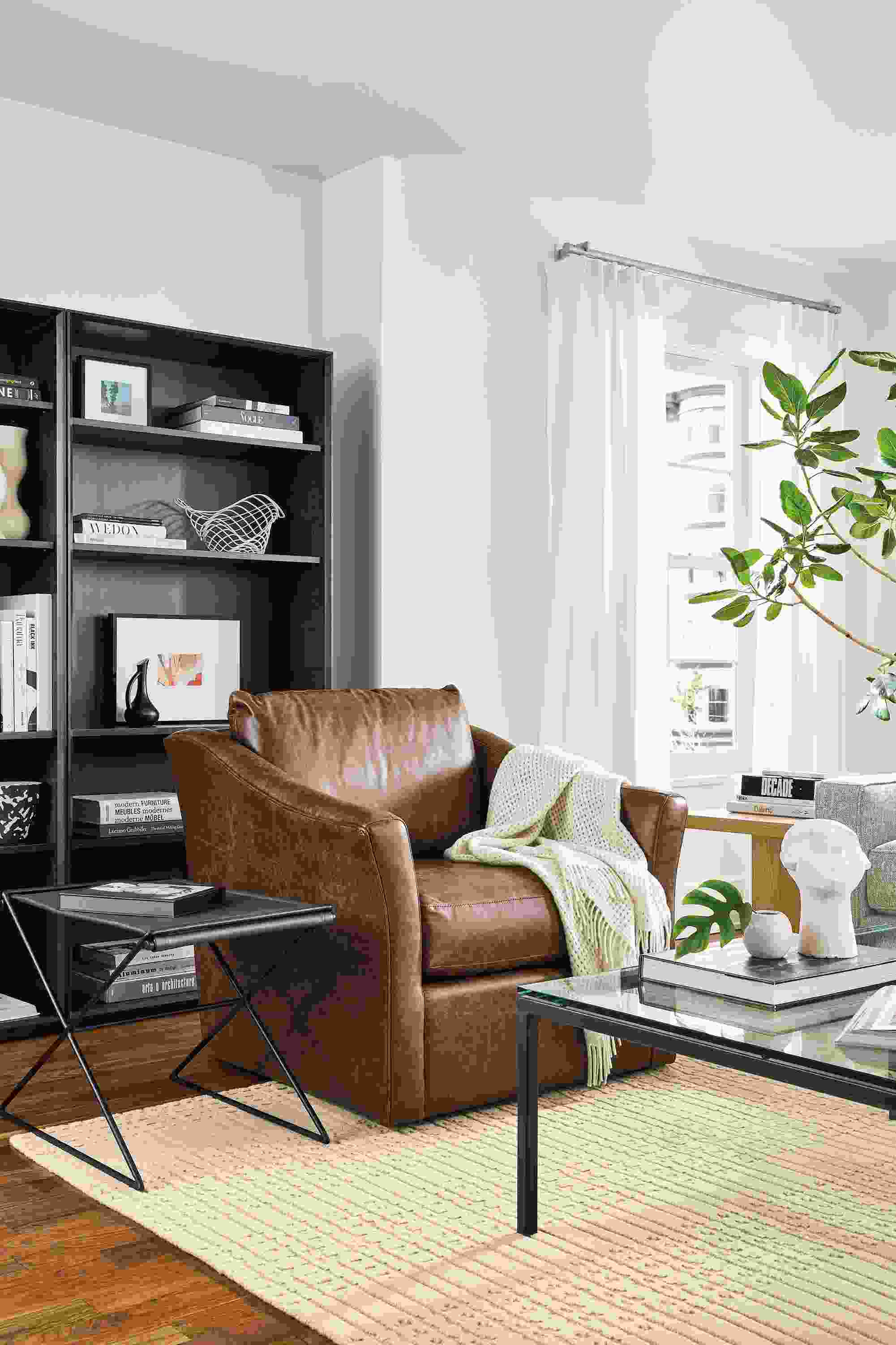 Living room with Maeve swivel chair in bourbon leather, tavi stool in black leather and rollins bookcases in charcoal.