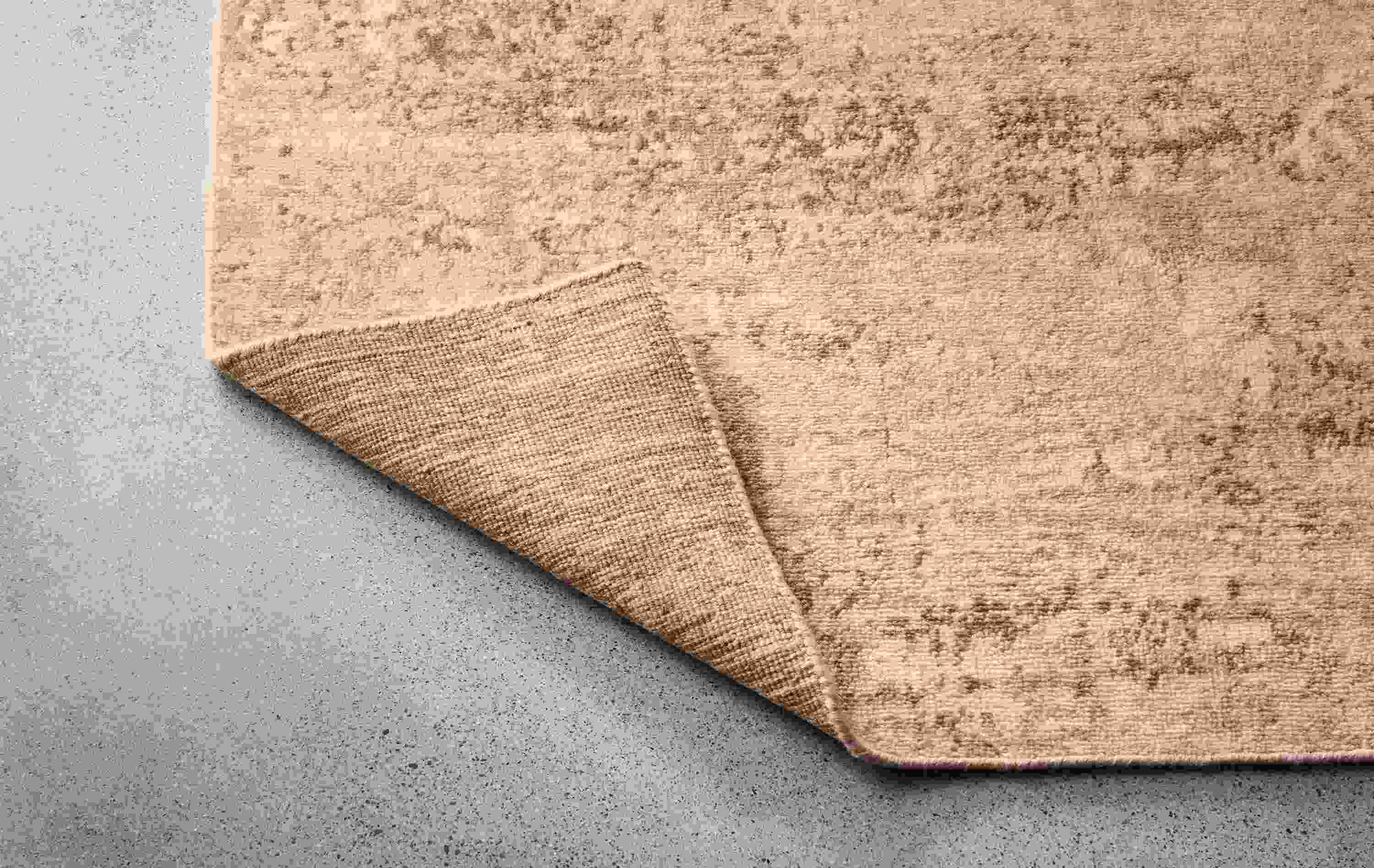 Makali 8 by 10 rug in stone shown with corner flipped up to show underside of rug.