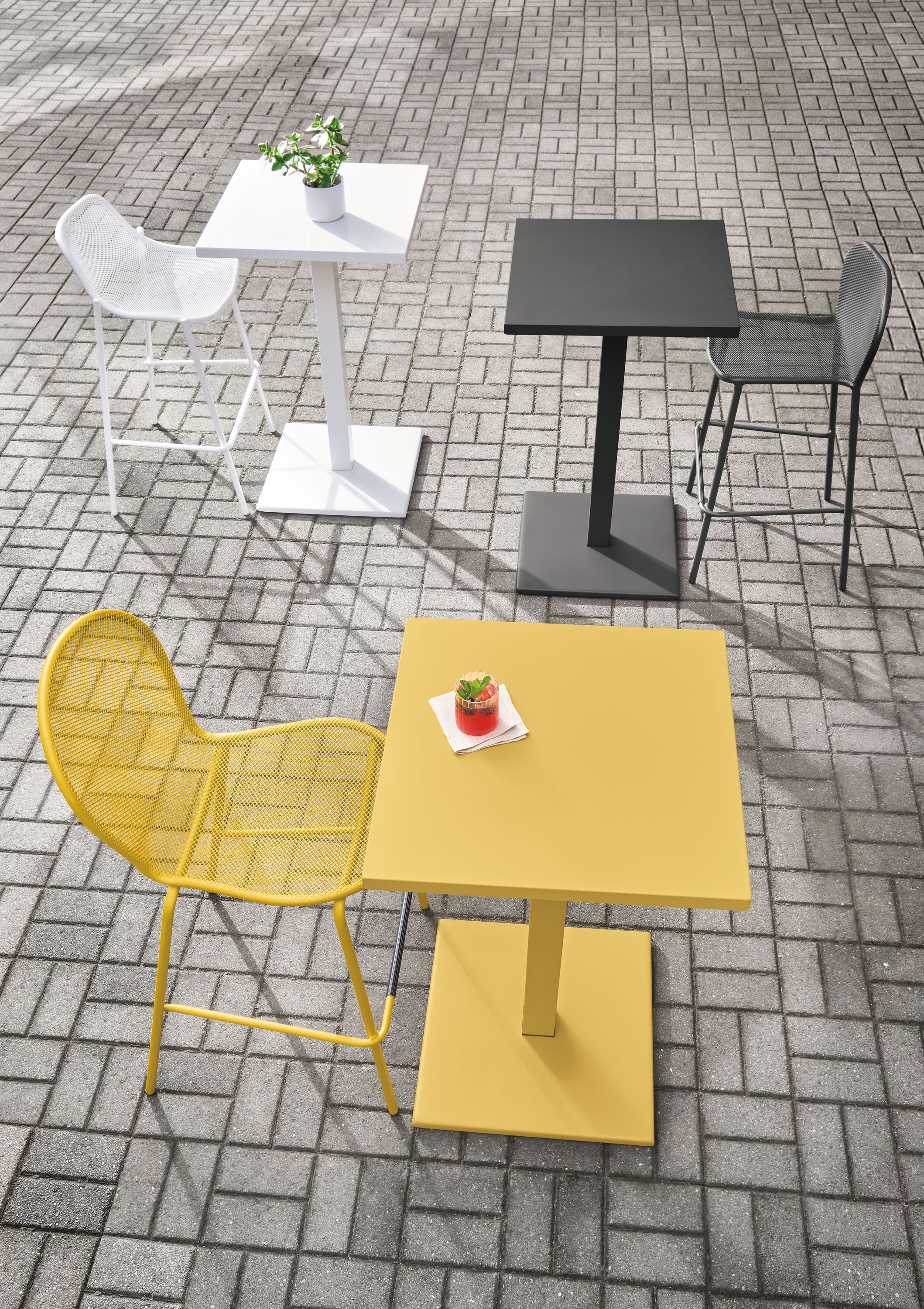 Maris square tables in saffron, graphite and white on a large brick patio.