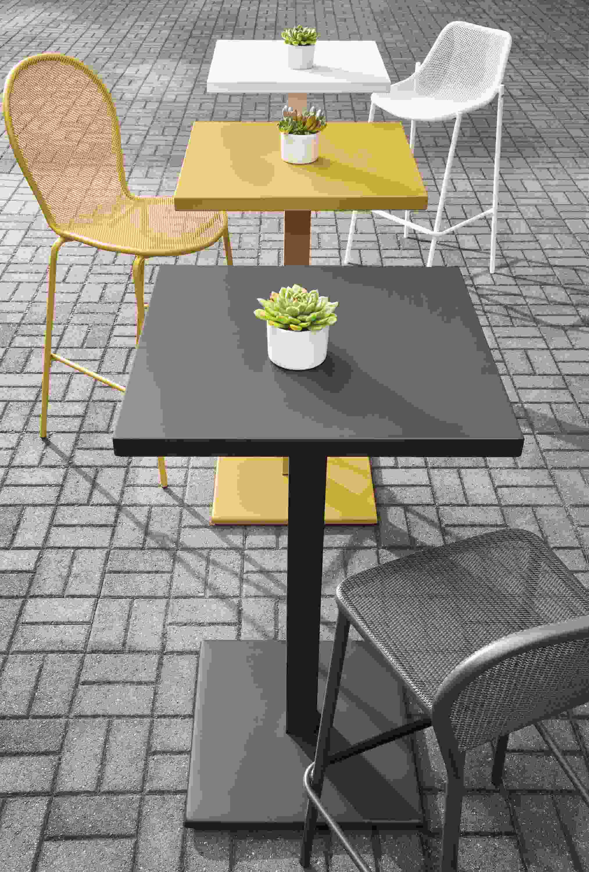 Maris tables in graphite, saffron and white on a brick patio.