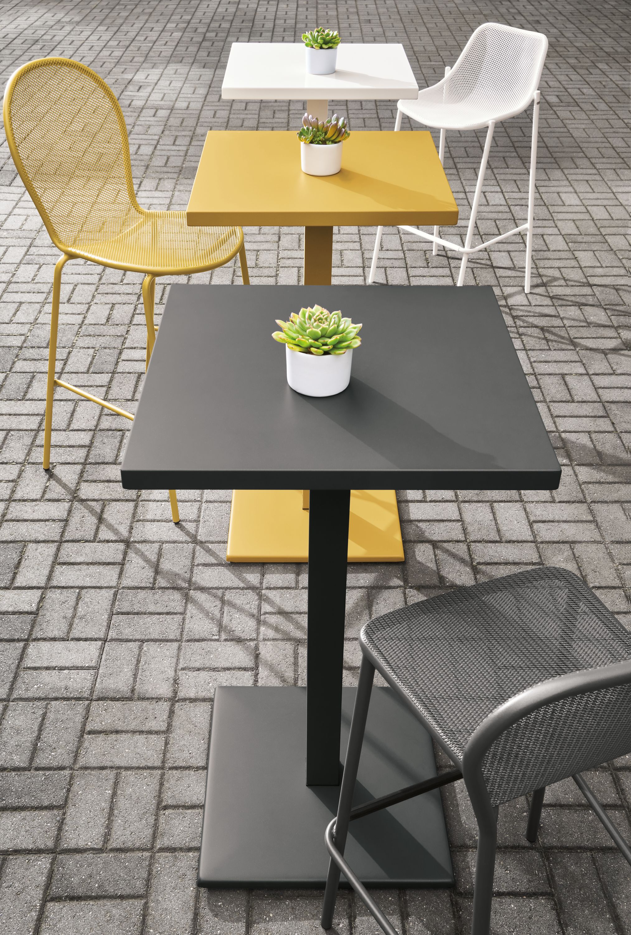 Maris tables in graphite, saffron and white on a brick patio.