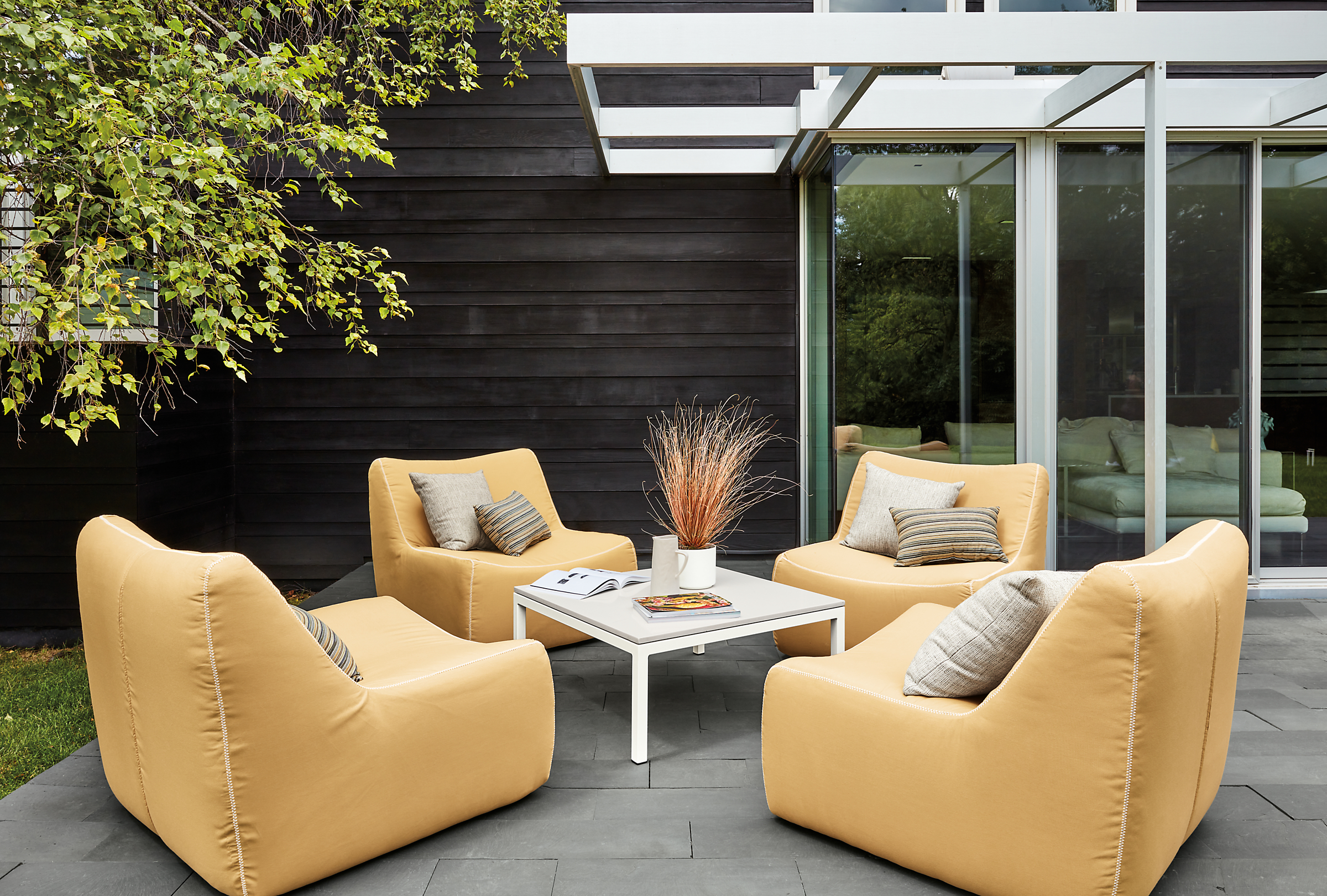 Outdoor setting with 4 Maya Swivel Chairs in Sunbrella Canvas Saffron and a Parsons 36 inch square outdoor coffee table.