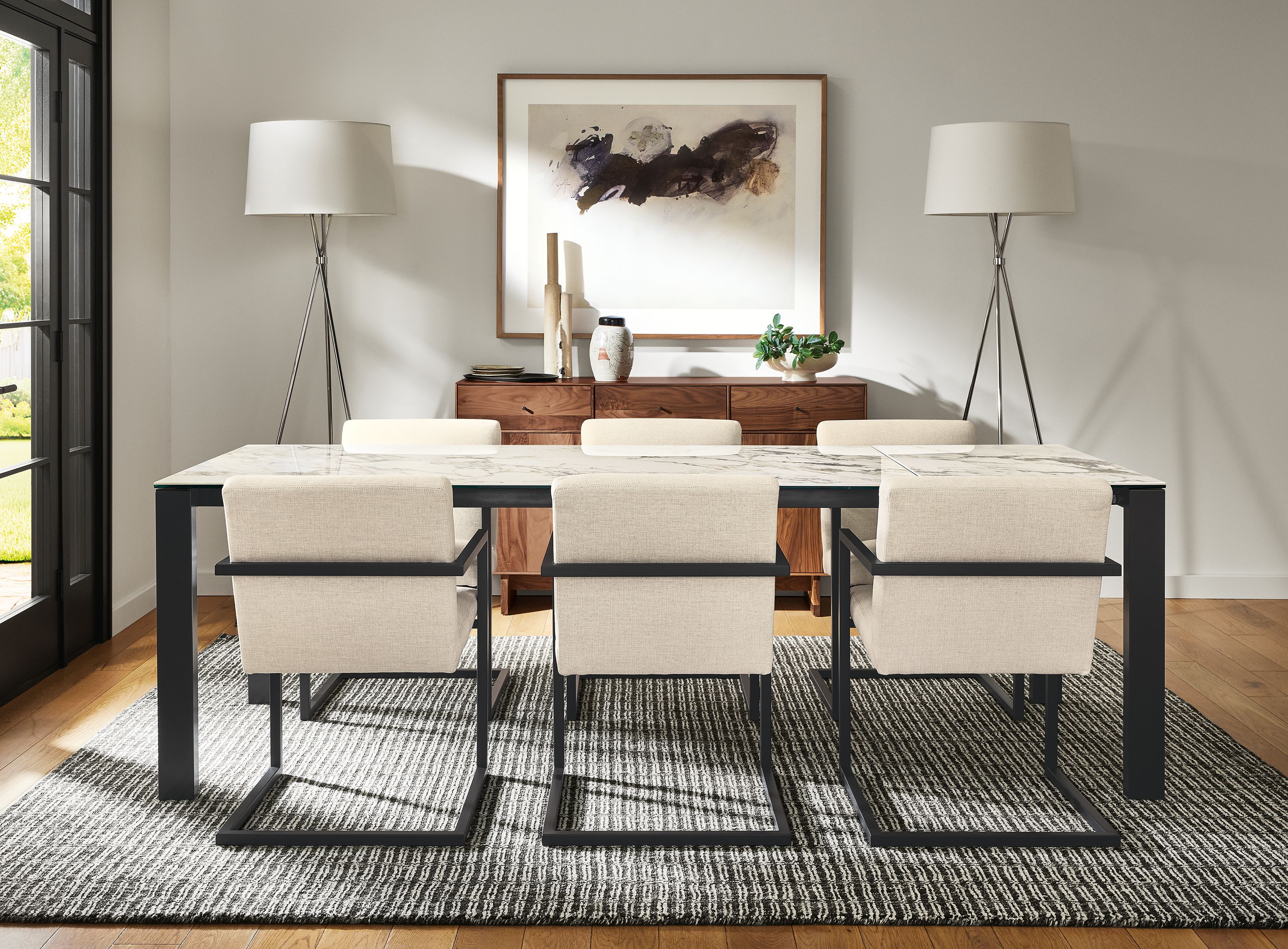 Dining room with Metric 72 wide extension table in graphite with marbled bright white ceramic top, Lira arm chair in Sumner Ivory, Nera 8 by 10 rug in coal, and two Tri-Plex floor lamp in polished nickel.