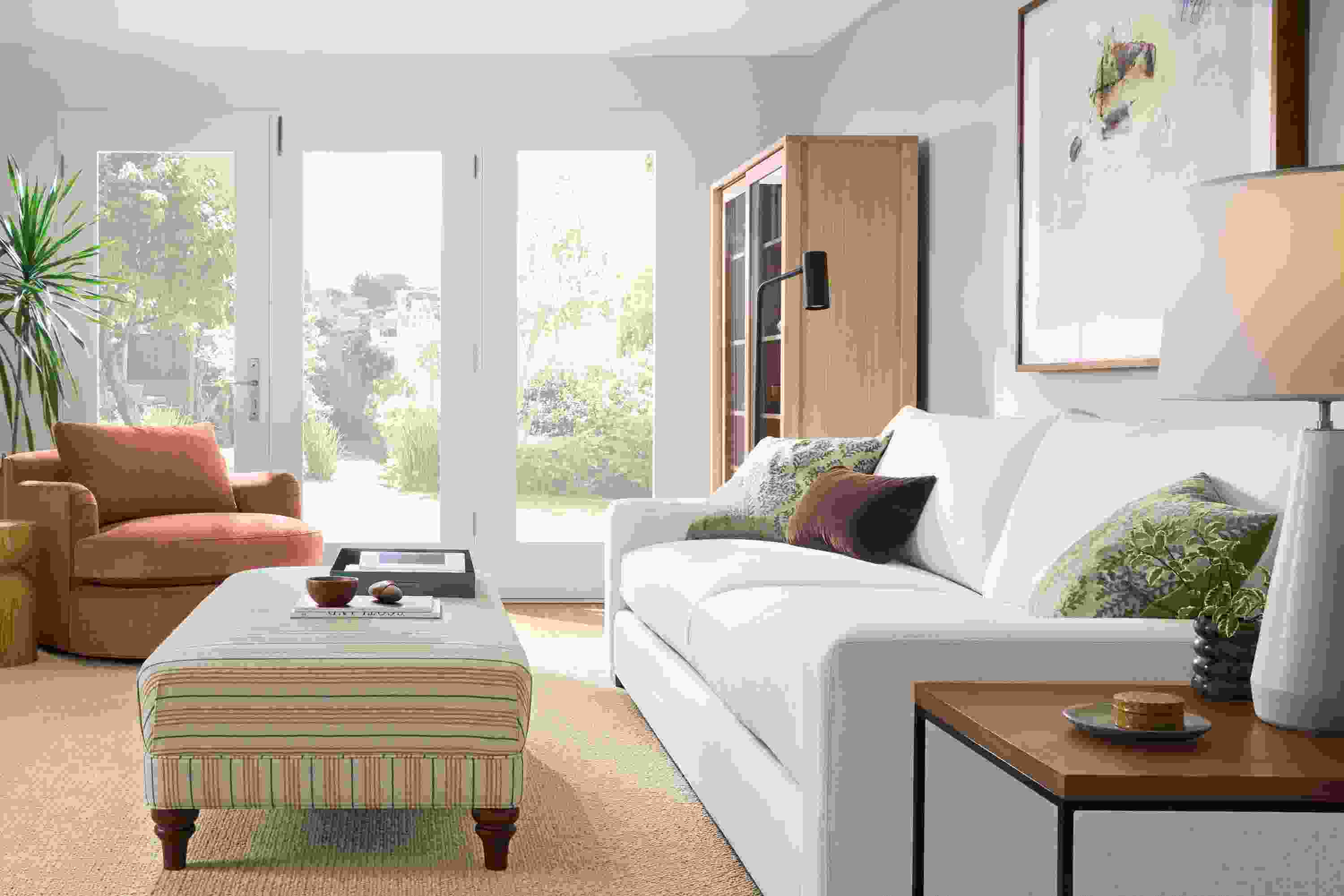 Living room with Metro deep 2-cushion sofa in Sumner Ivory, Humphrey ottoman in Prescott Natural and Flannery rug in oatmeal.