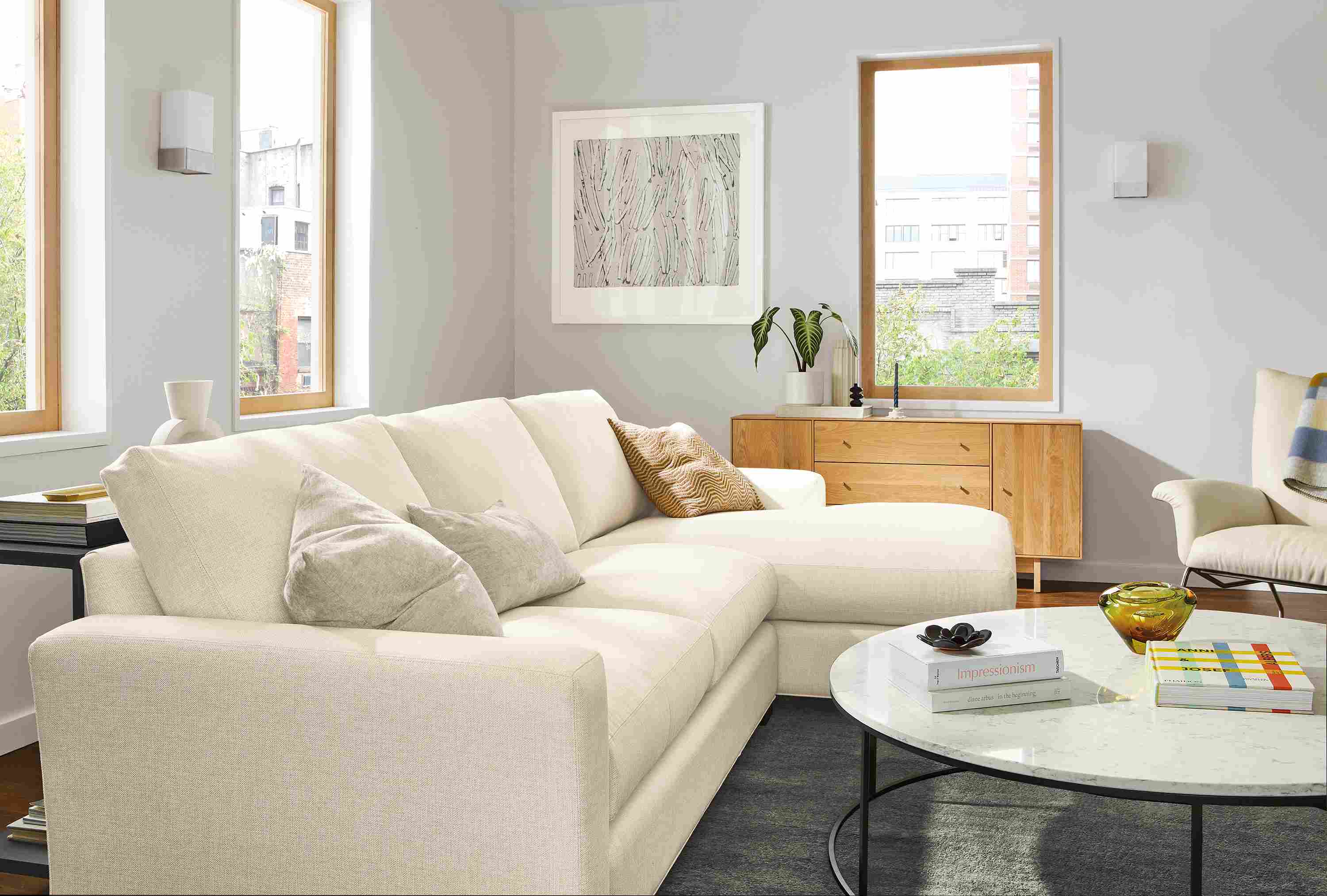 Living room with Metro sofa with right-arm chaise in Sumner Ivory, Tyne 48-round coffee table and Hudson storage cabinet in White Oak.