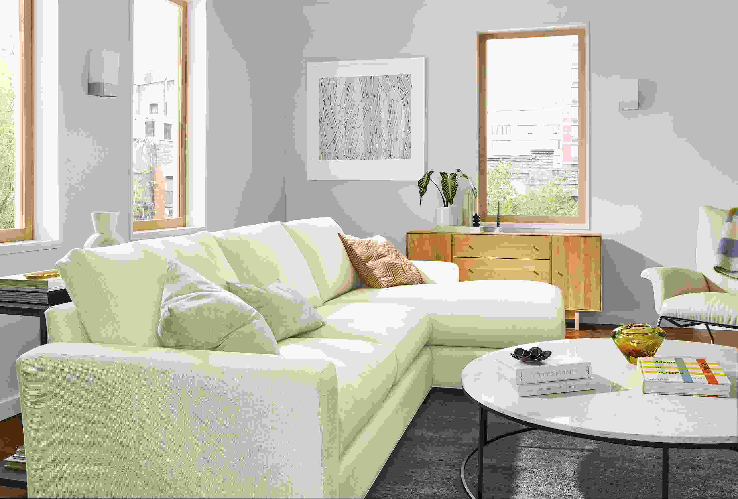 Living room with Metro sofa with right-arm chaise in Sumner Ivory, Tyne 48-round coffee table and Hudson storage cabinet in White Oak.