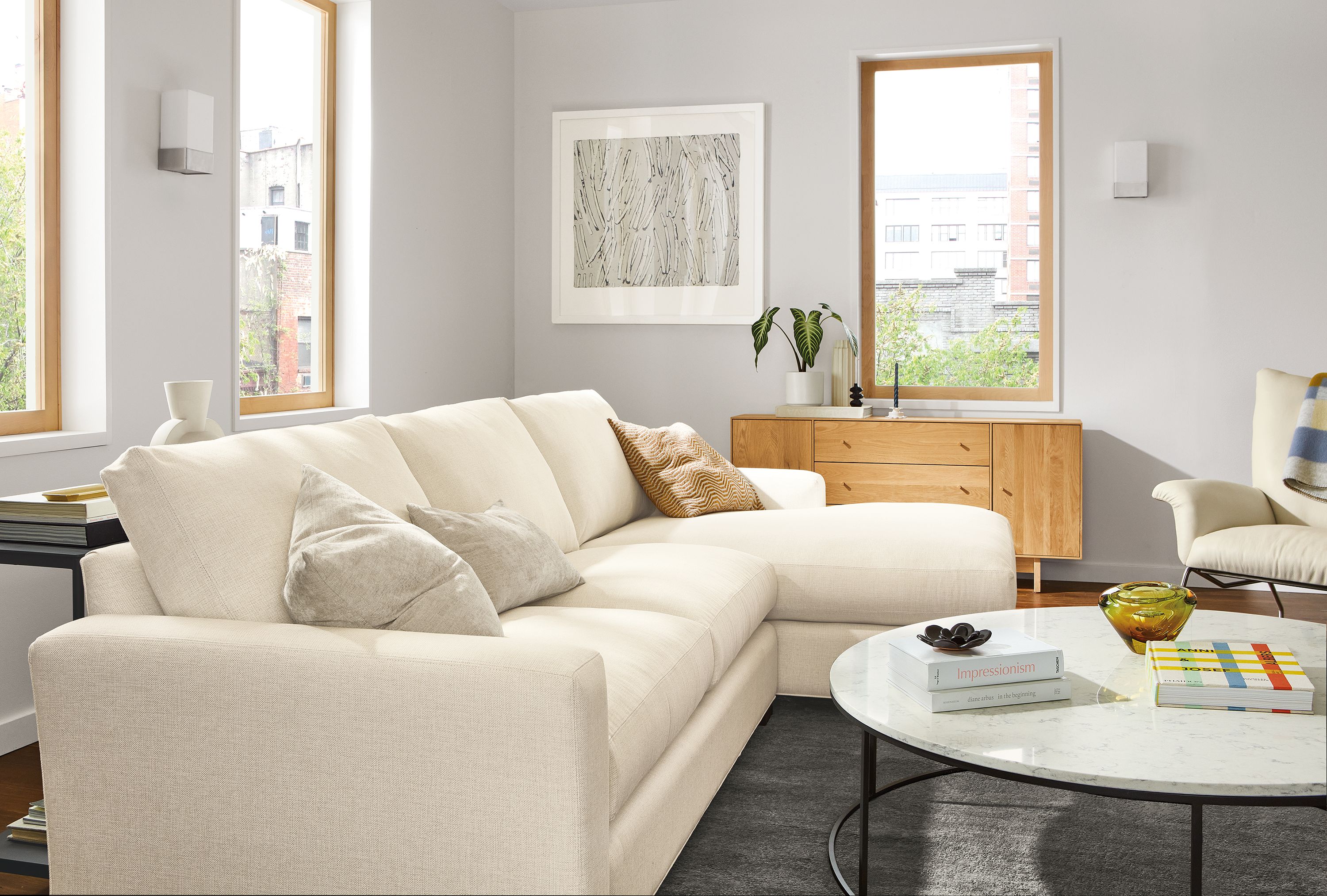 Living area with Metro sofa and right-arm chaise in Sumner Ivory, Tyne 48-round coffee table and Hudson storage cabinet in White Oak.