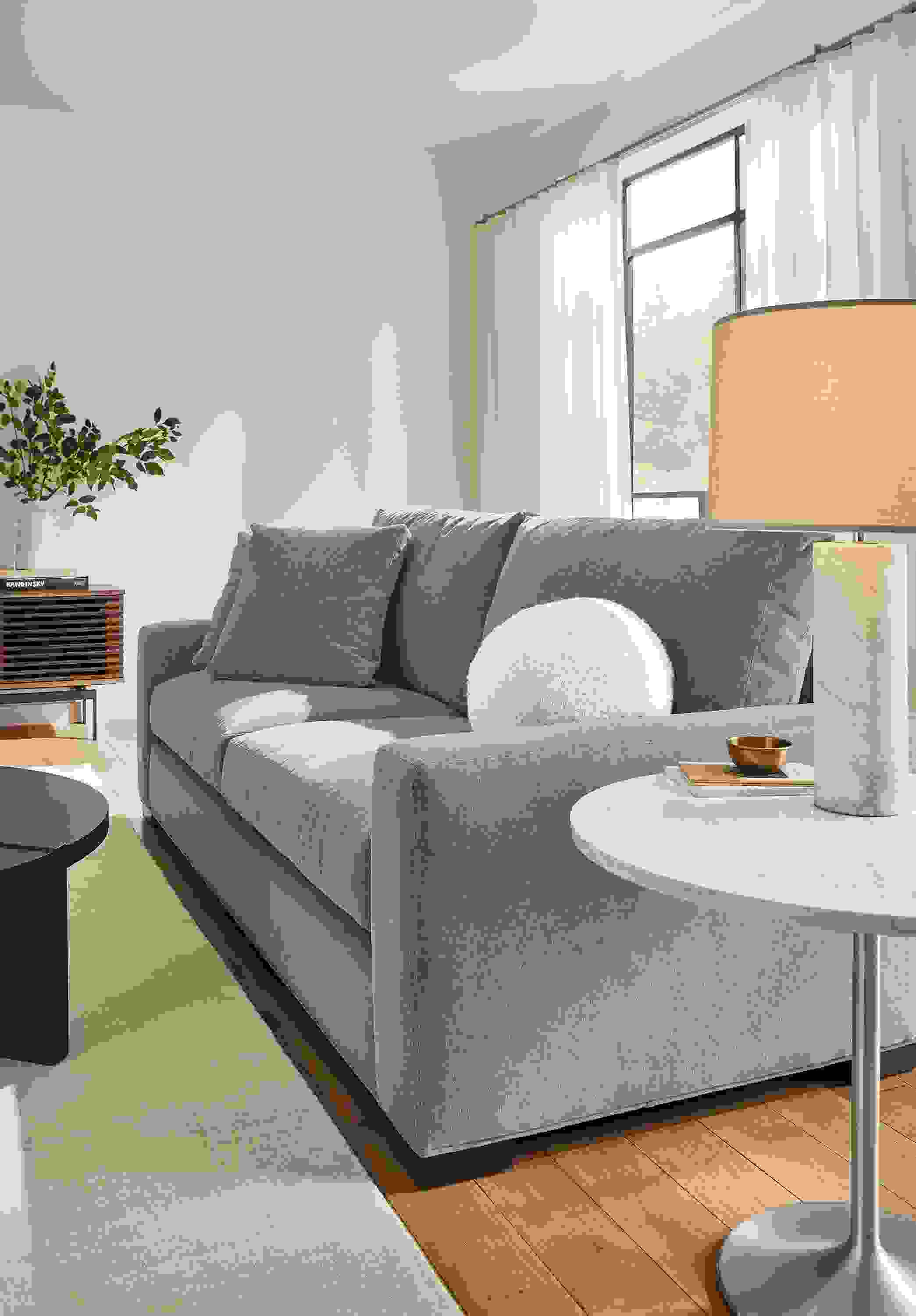 Living room setting with Metro 88-inch Sofa in Vick lead fabric, Aria 27-round end table in stainless steel with Marbled with quartz top and Ionic table lamp in with white marble base.
