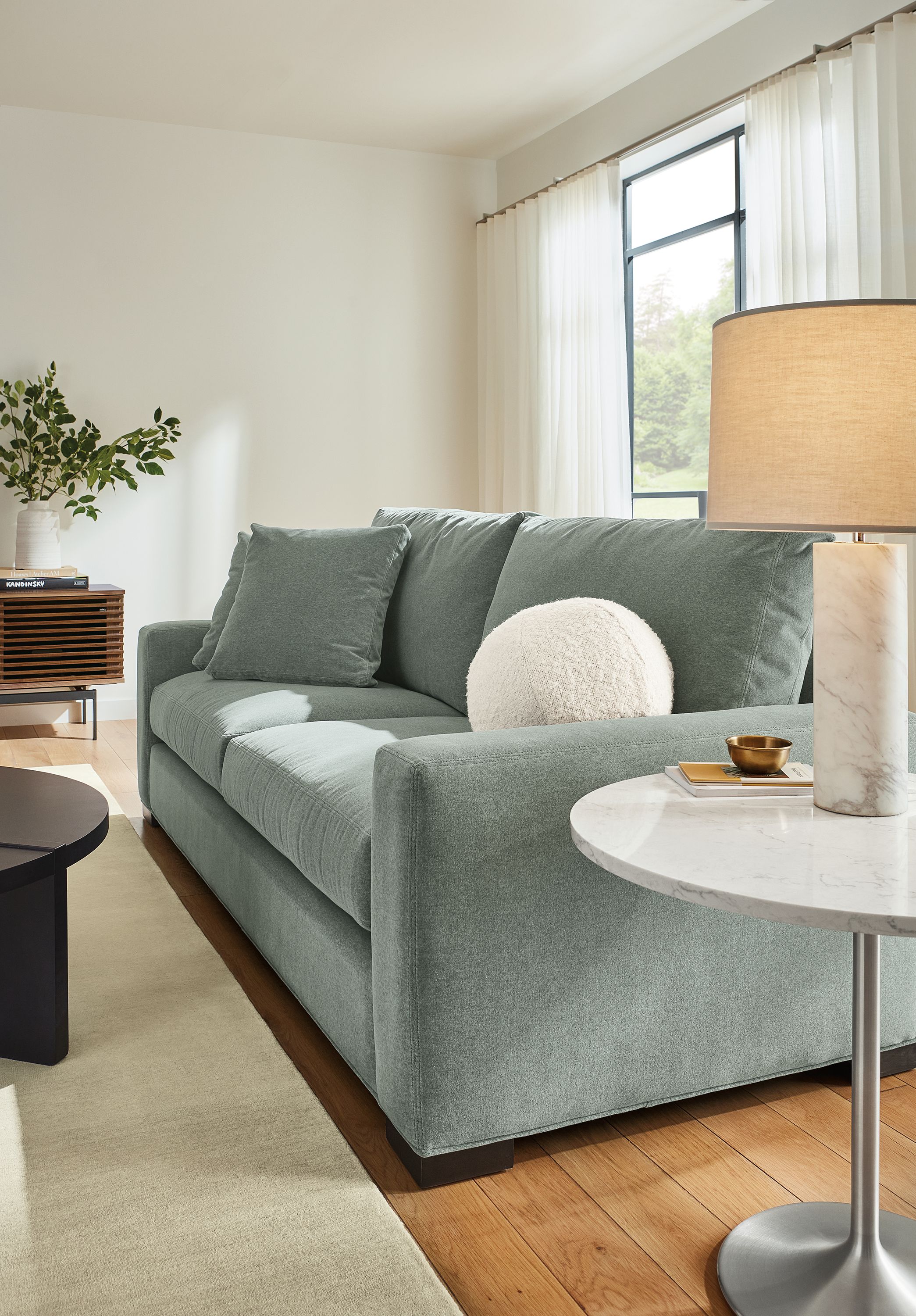 Living room setting with Metro 88-inch Sofa in Vick lead fabric, Aria 27-round end table in stainless steel with Marbled with quartz top and Ionic table lamp in with white marble base.