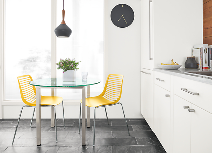 Dining area with Mini side chairs in yellow with chrome legs and Parsons 36-round table in Stainless steel and glass.