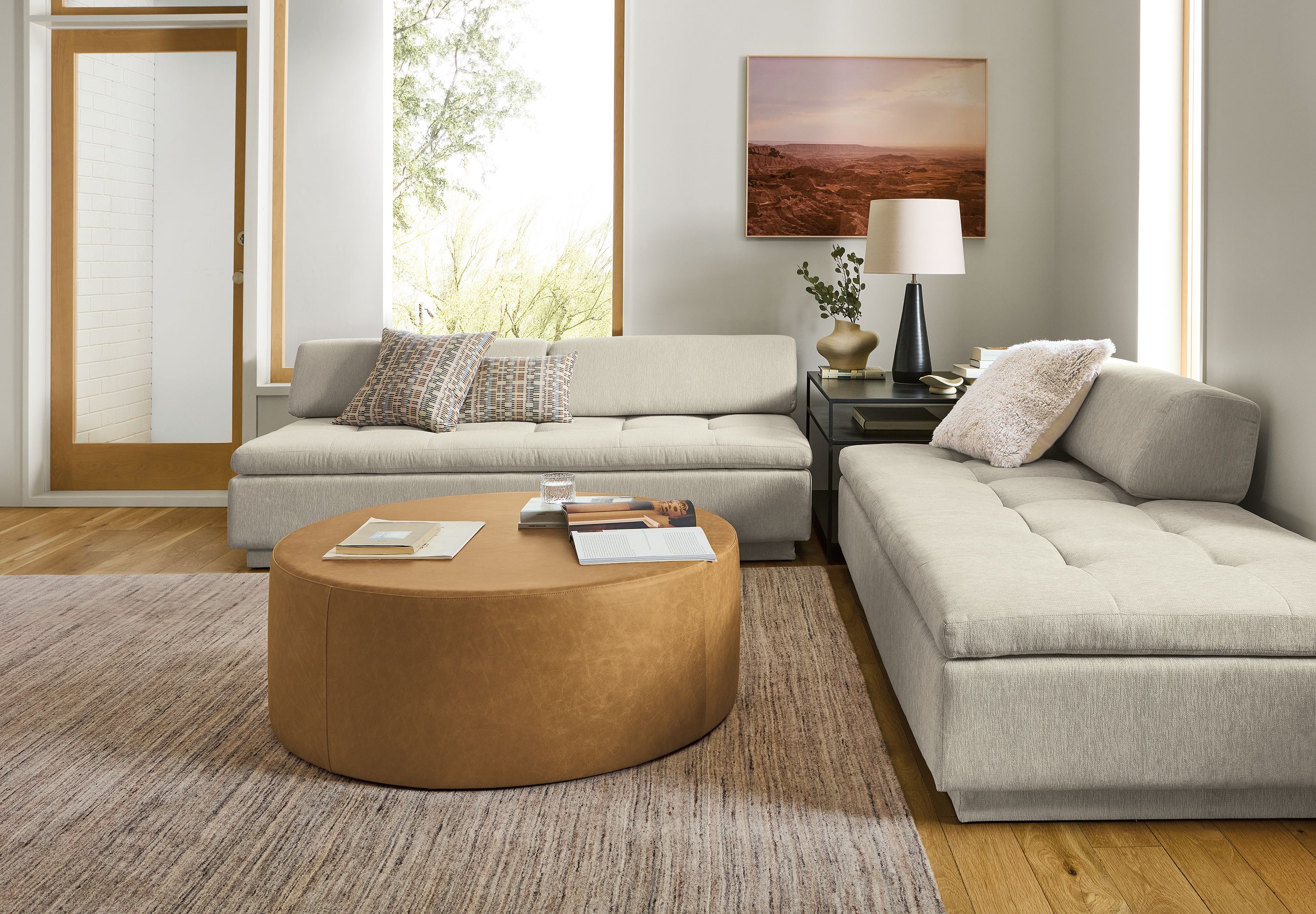 Living room 2 Miranda daybeds in crawford bone, slim end table in natural steel and Aero round ottoman in Palermo Camel leather.