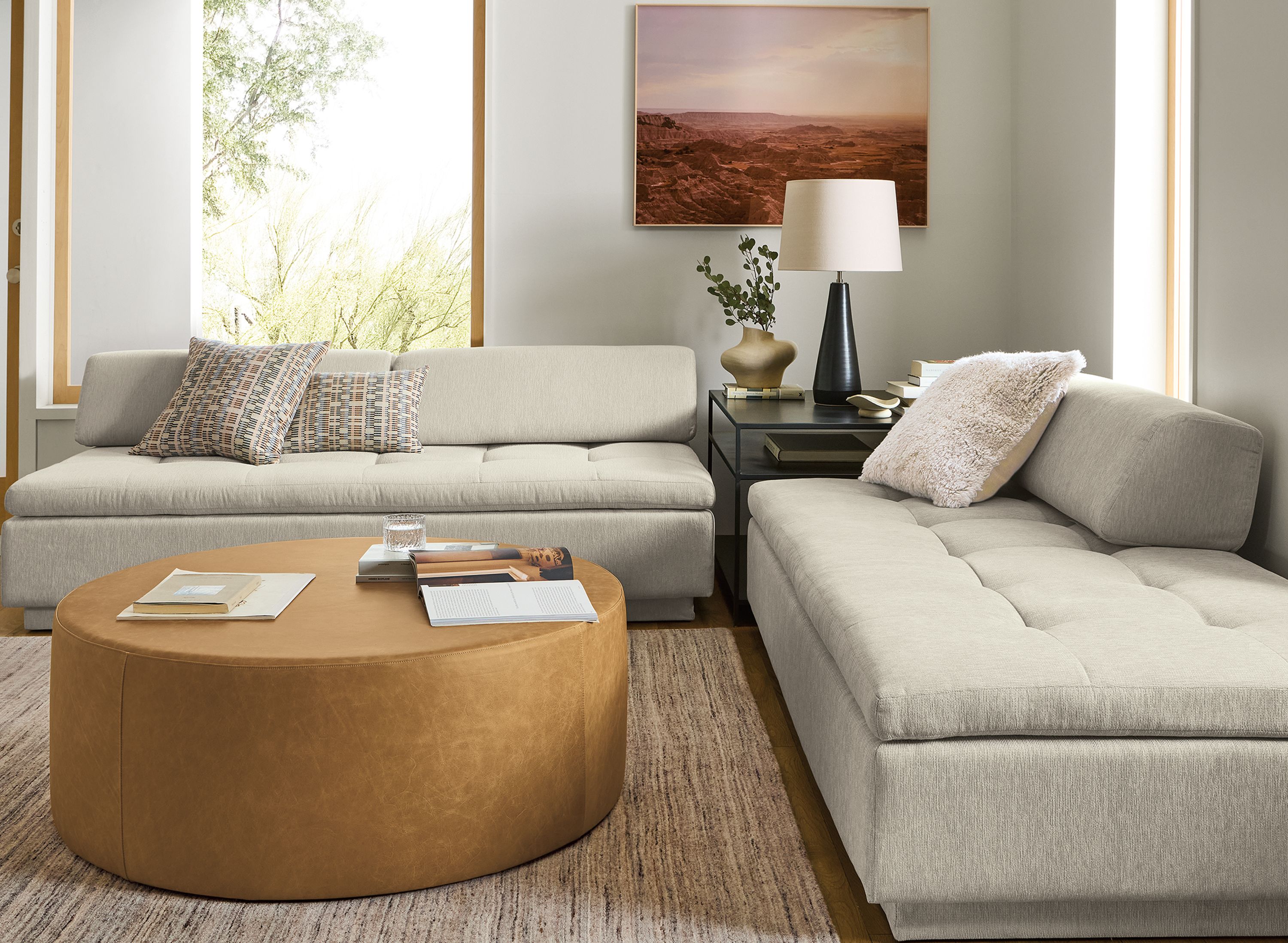 Living room 2 Miranda daybeds in crawford bone, slim end table in natural steel and Aero round ottoman in Palermo Camel leather.