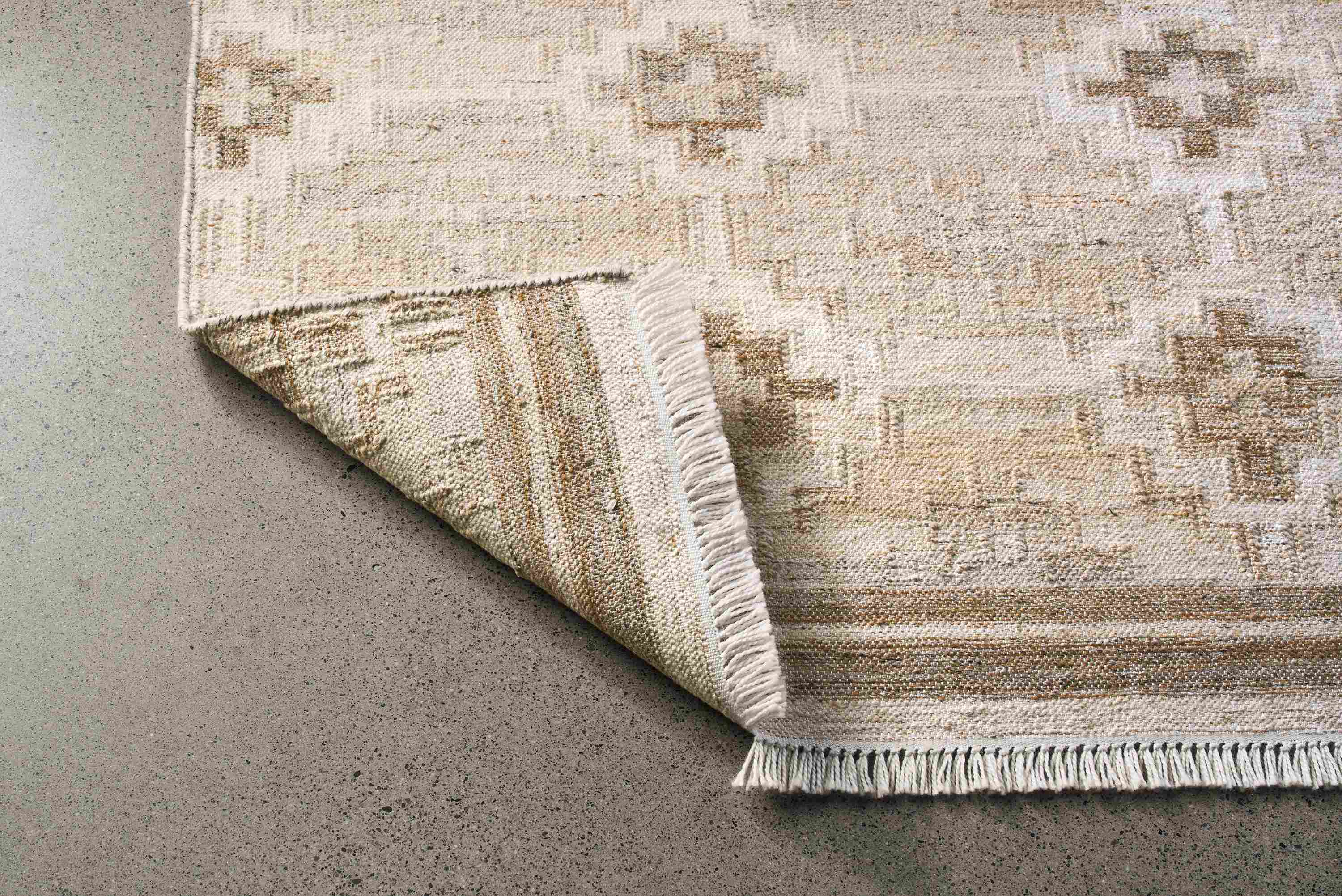 Detail of the upturned corner on a mojave 8 by 10 rug in sand.
