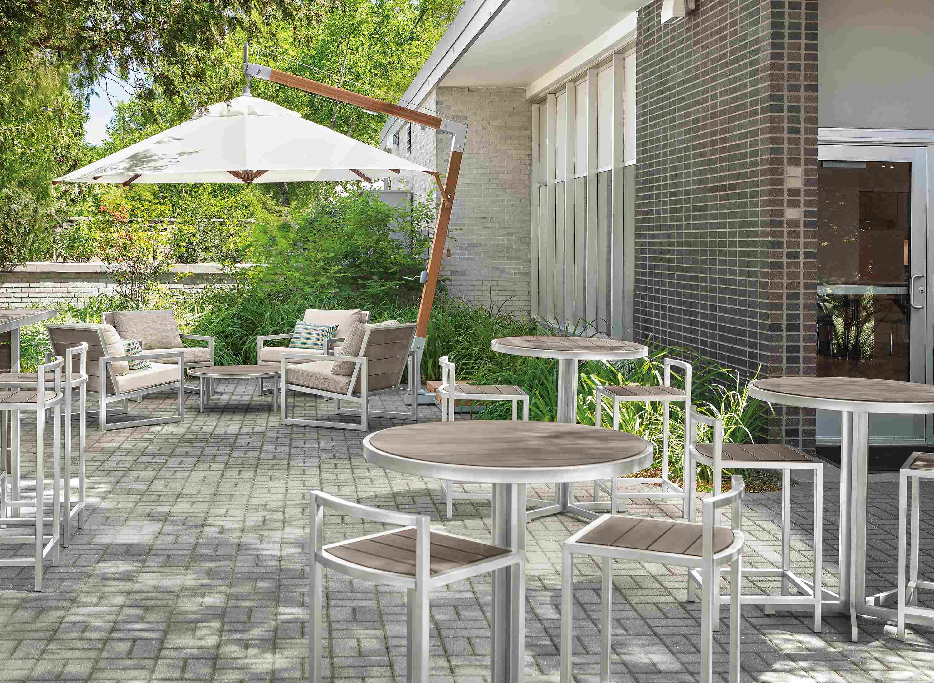 Outdoor dining area with Cumulo patio umbrella, Montego chairs, tables, stools in aged thermally modified oak.