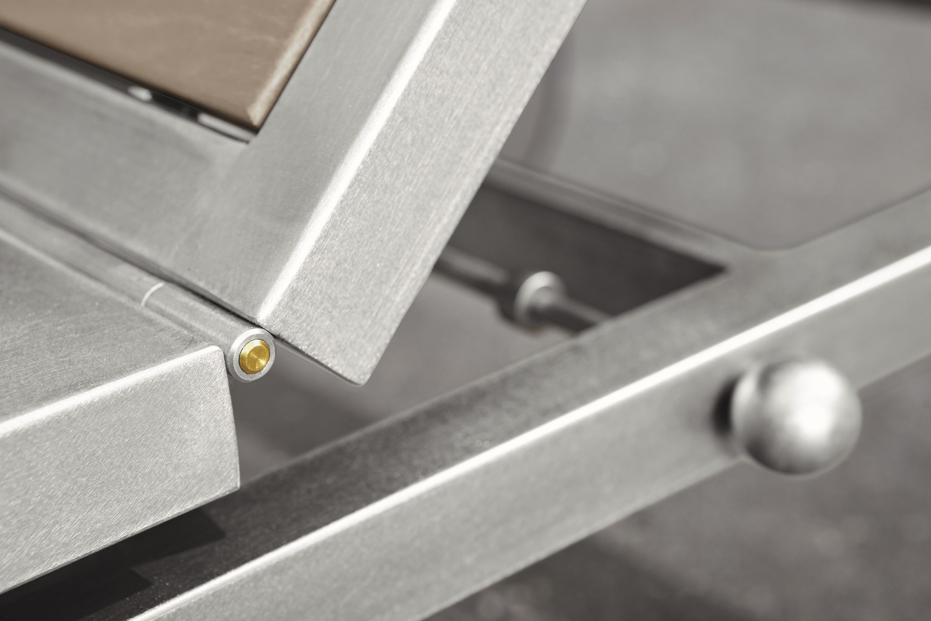 Close detail of seat hinge on a Montego chaise in stainless steel and aged thermally modified oak.