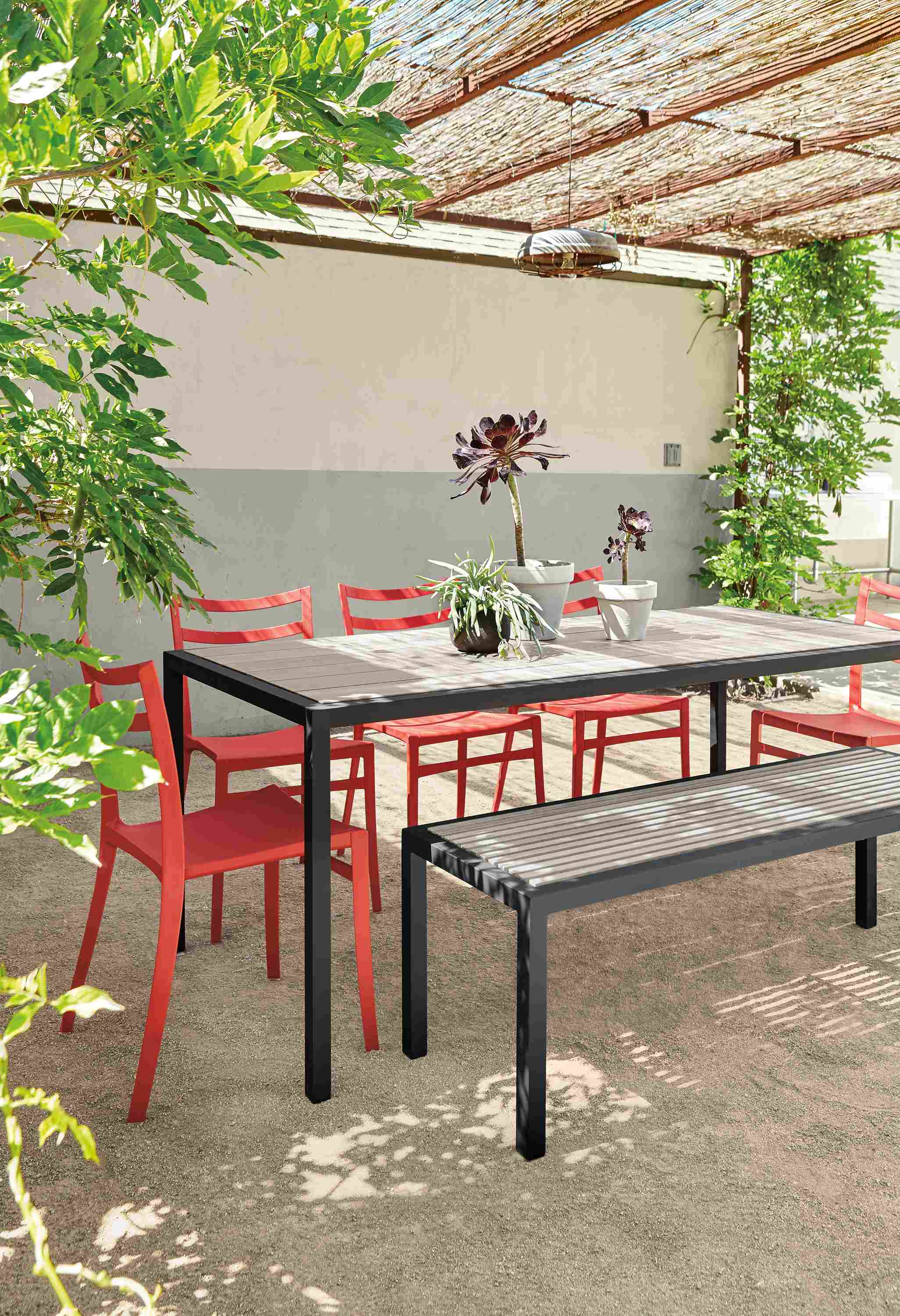 Patio with Montego table and bench in graphite and aged thermally modified ash and 5 Sabrina chairs in red.
