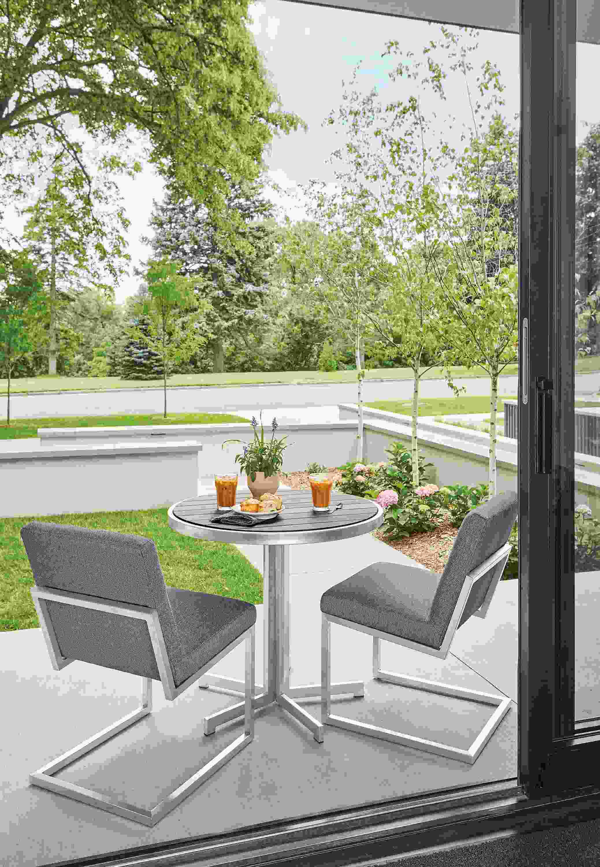 Outdoor patio with finn side chairs in mist fabric and Montego round table in aged thermally modified oak and stainless steel.