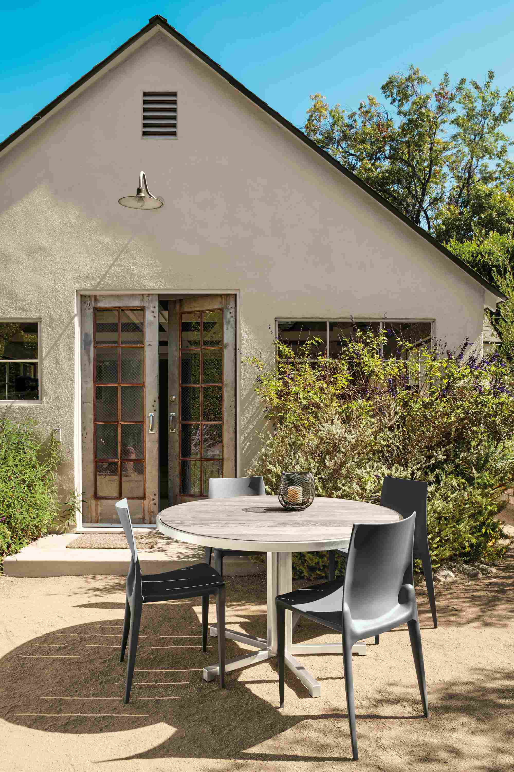 Outdoor space with Montego bar table in stainless steel and aged thermally modified ash and 4 Bellini chairs in dark grey.