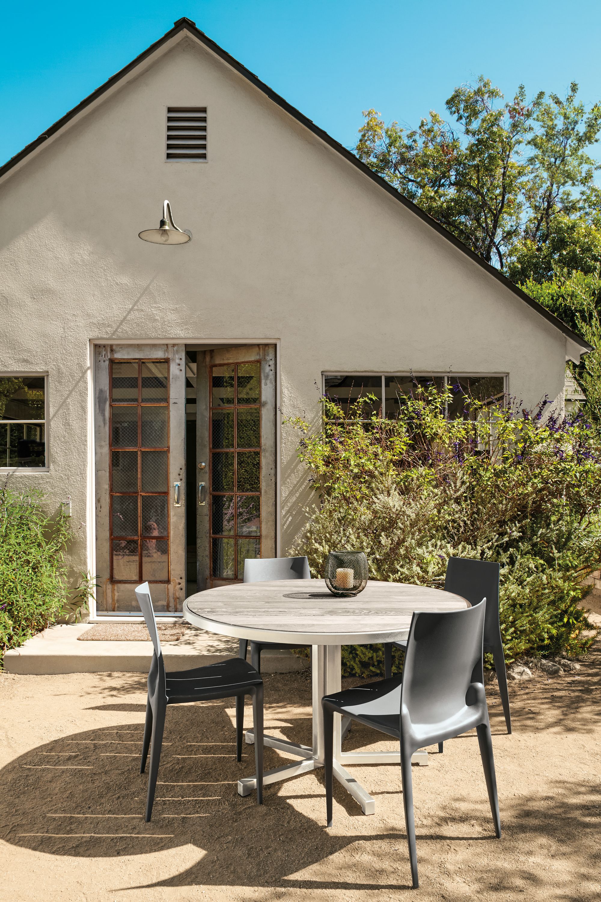 Outdoor space with Montego bar table in stainless steel and aged thermally modified ash and 4 Bellini chairs in dark grey.