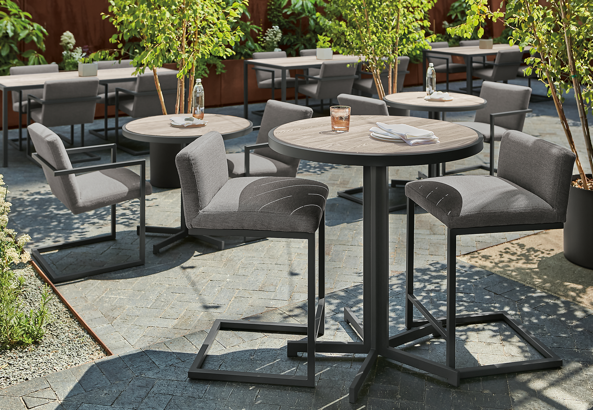 detail of aged thermally modified ash montego round counter tables and finn counter stools in outdoor space.