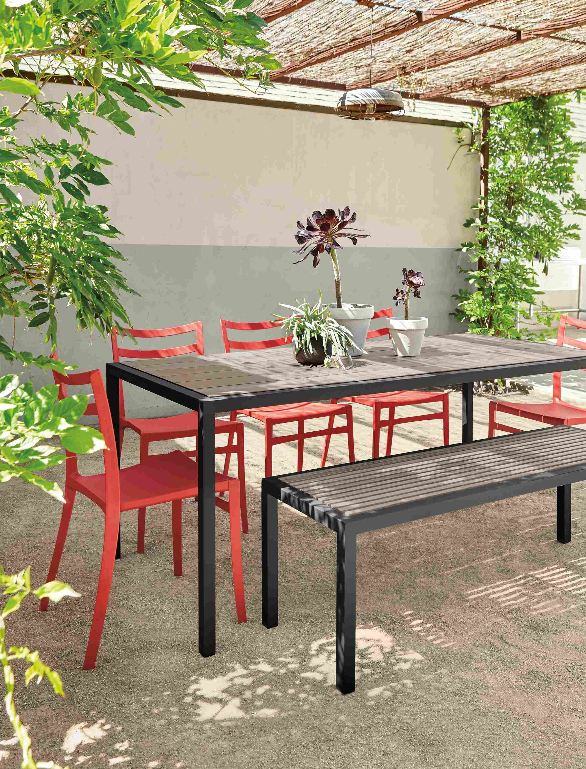 Outdoor patio space with Montego table and bench in aged thermally modified oak and graphite and Sabrina chairs in red.