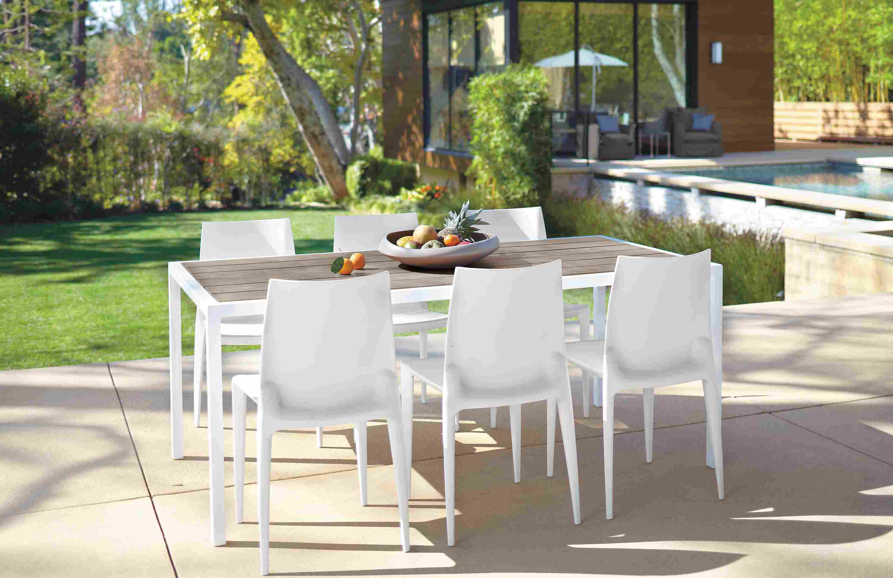Dining patio near a pool with Montego table in aged thermally modified oak and white and 6 Bellini chairs in white.
