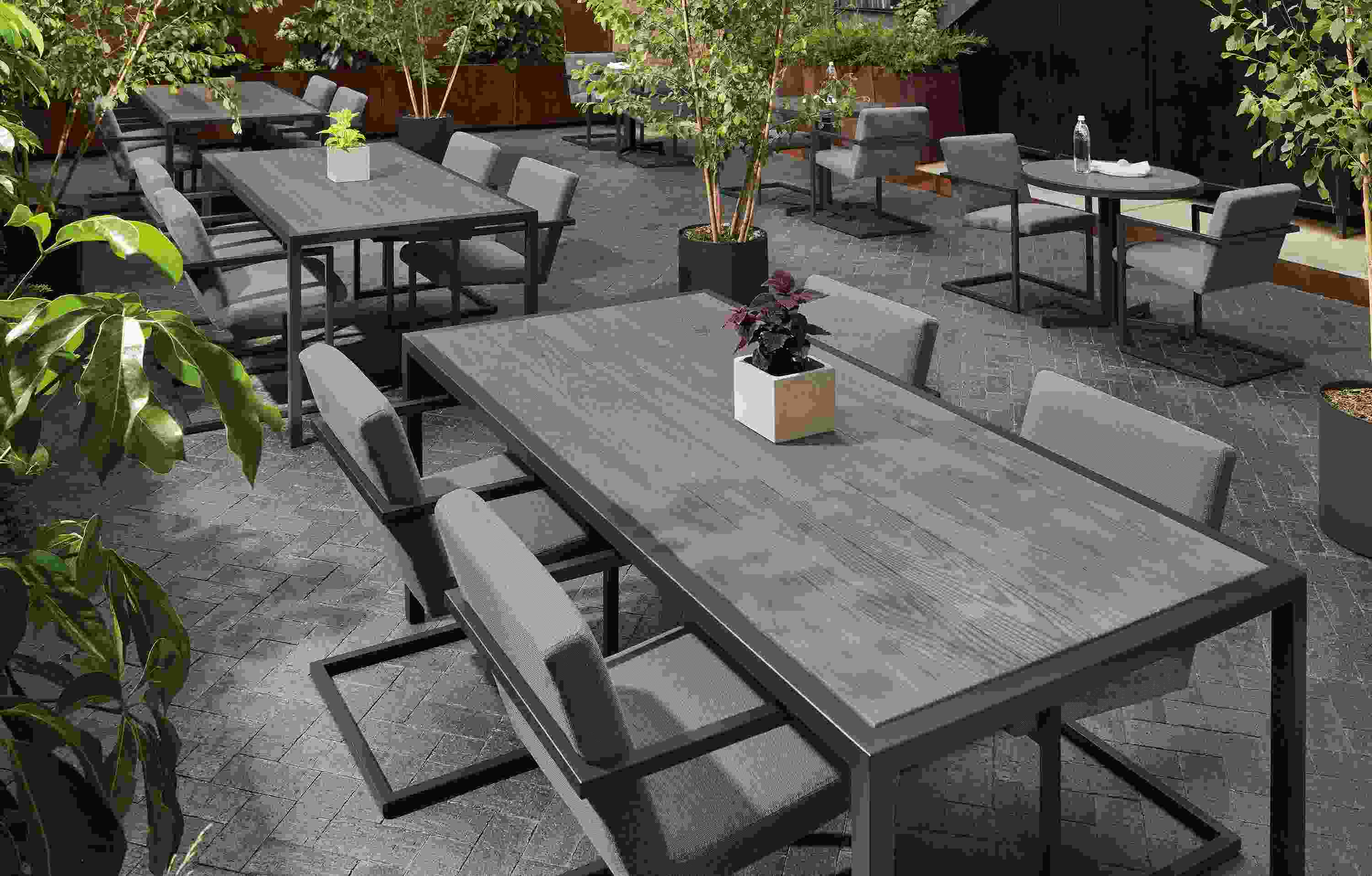Outdoor commercial dining space with several Montego tables in aged thermally modified oak and graphite and 18 Finn arm chairs.