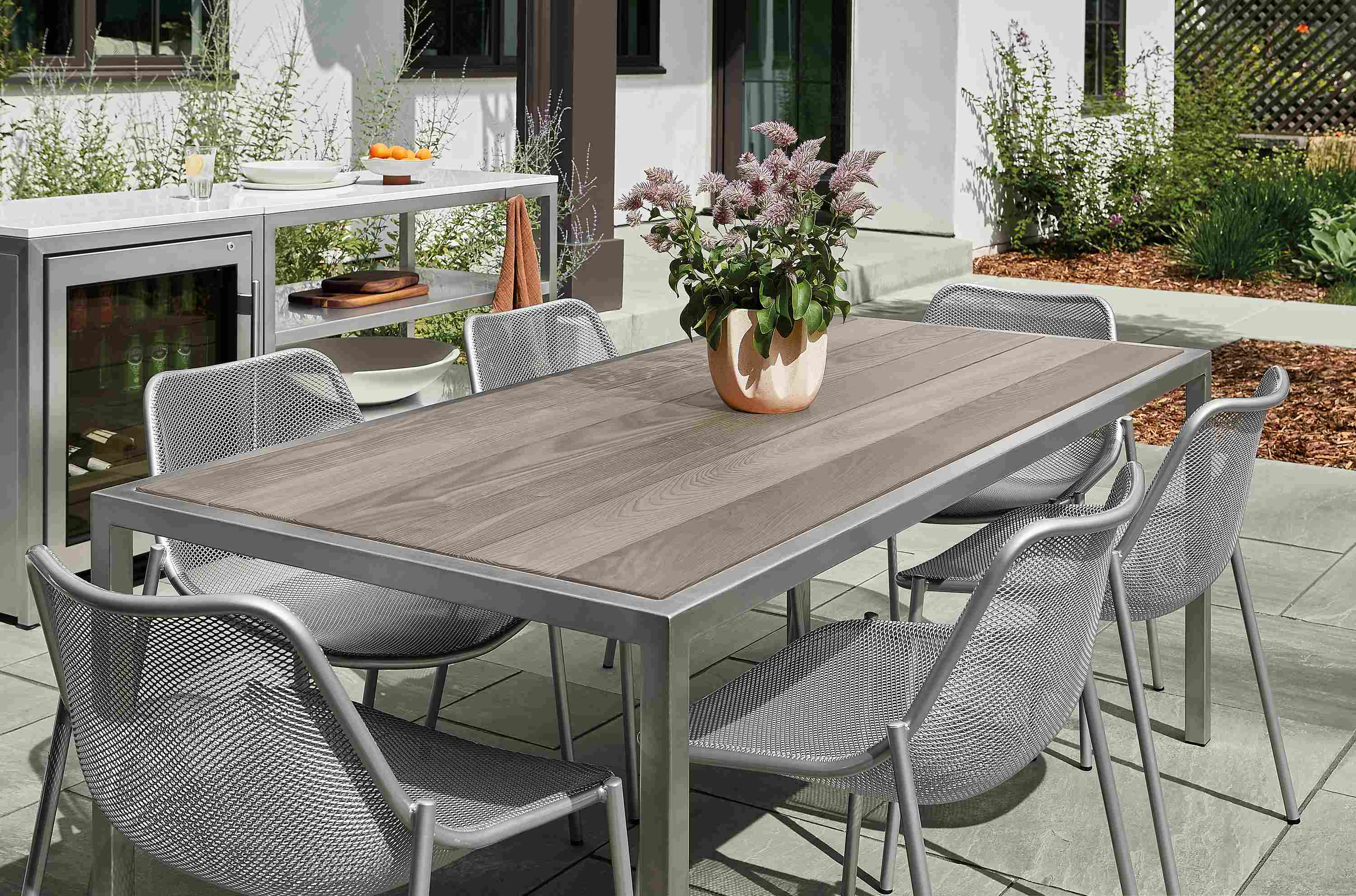 Outdoor space with montego dining table in aged thermally modified oak and six soleil side chairs in stainless steel.