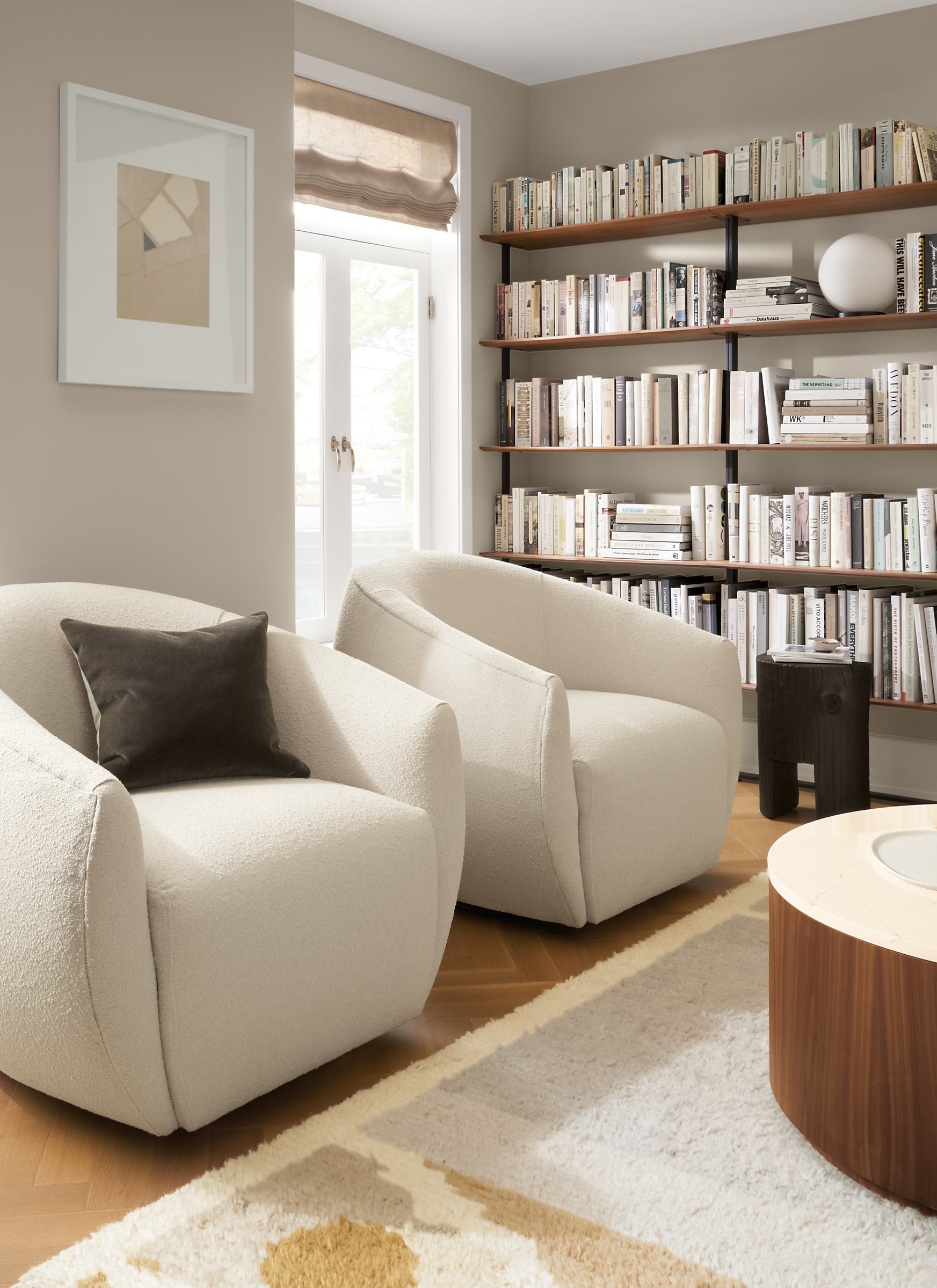 Room setting with two Mora swivel chairs with  Liam 36-round Coffee Table in Walnut and Beam bookshelves line the wall.