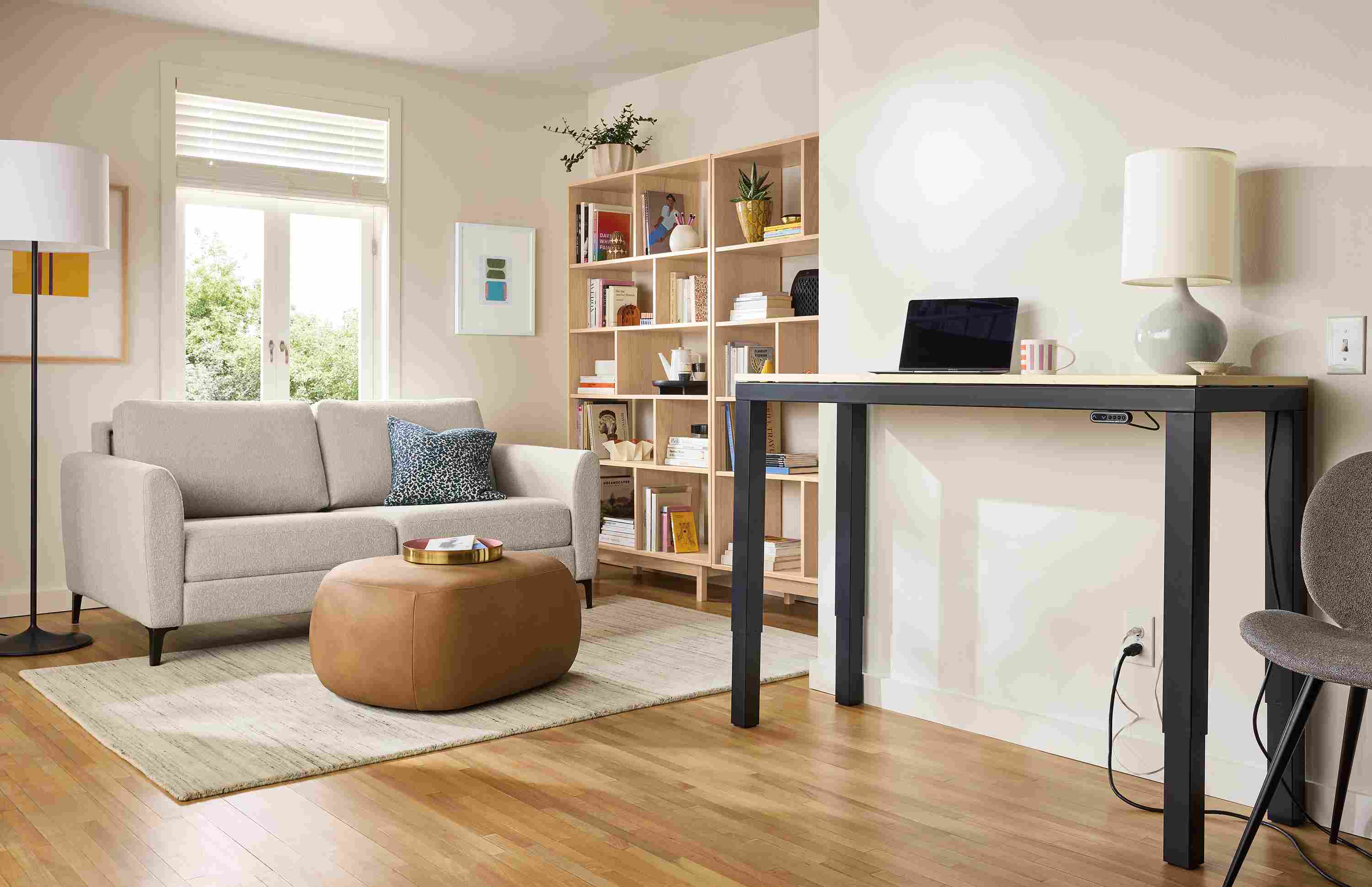 Large open room with Natalia queen sleeper sofa in Conley Natural and Parsons adjustable standing desk shown in up position.