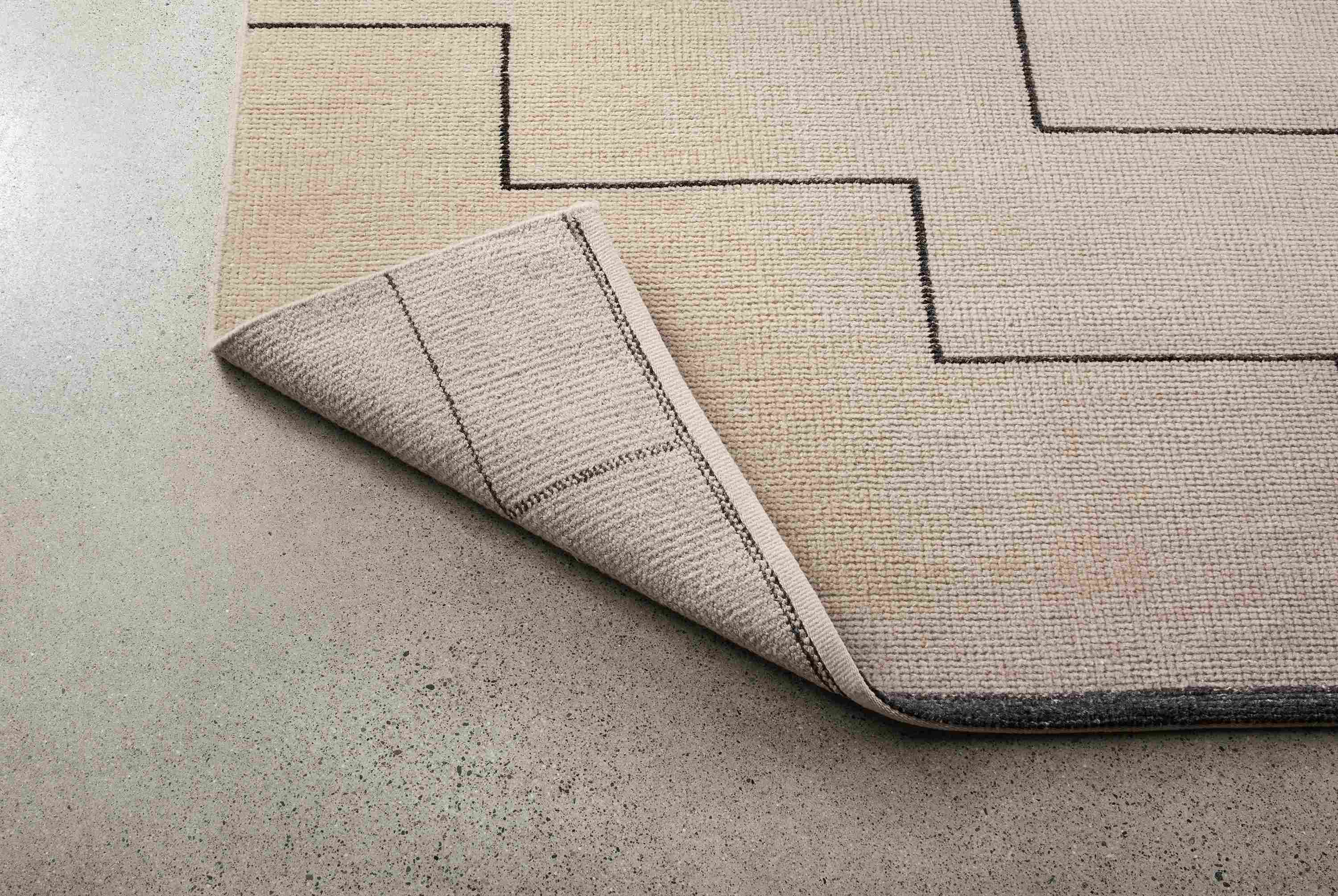 Navi 8 by 10 rug in ivory/black shown with corner turned up to show underside of rug.