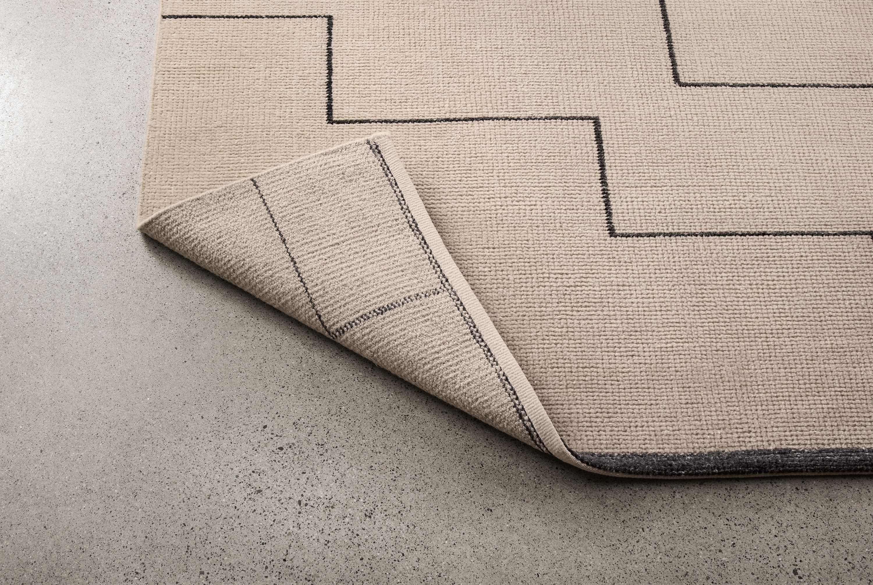 Navi 8 by 10 rug in ivory/black shown with corner turned up to show underside of rug.