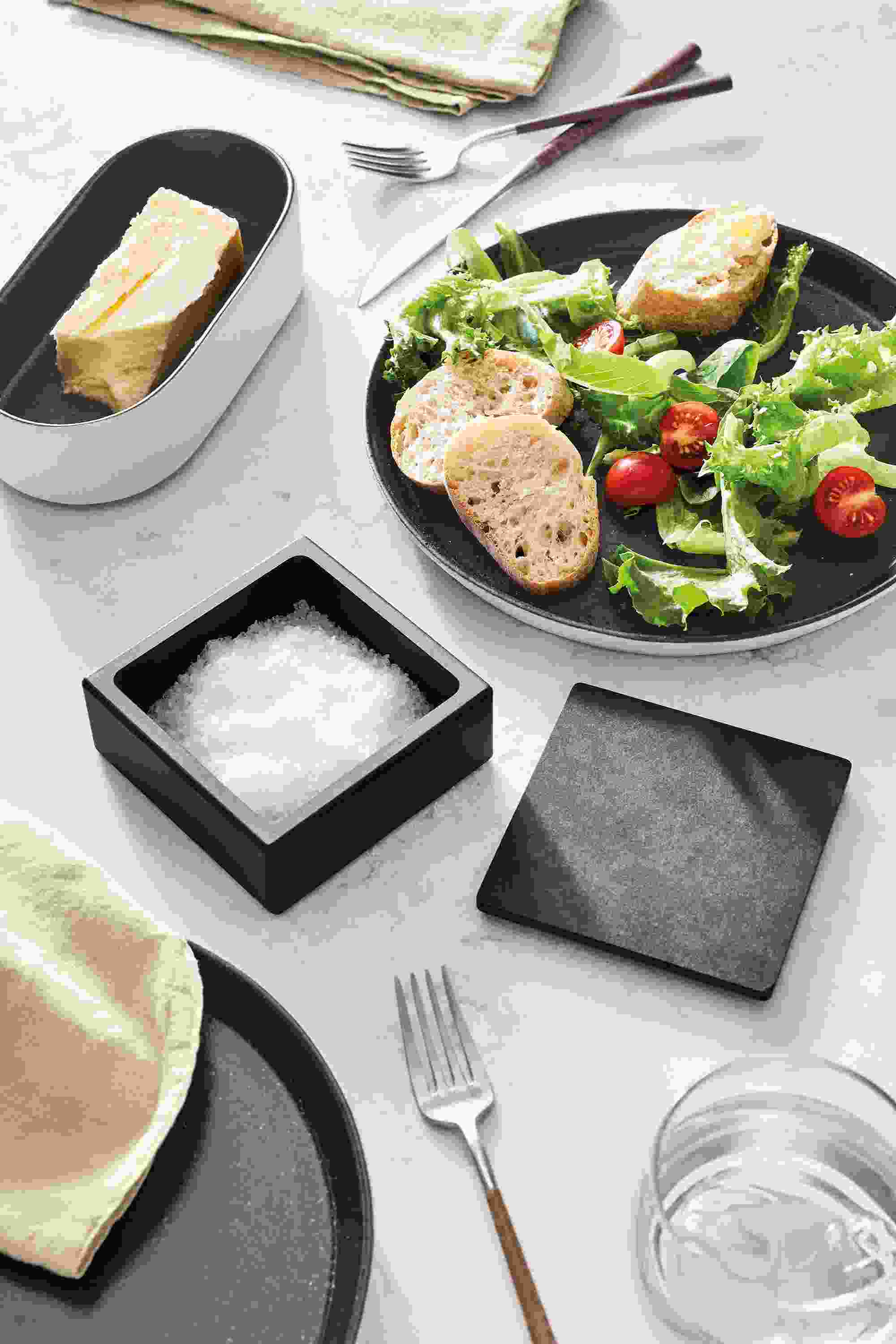 Tabletop with Nikko salt cellar in slate, Notos plate, Notos oval tray and Mito flatware.