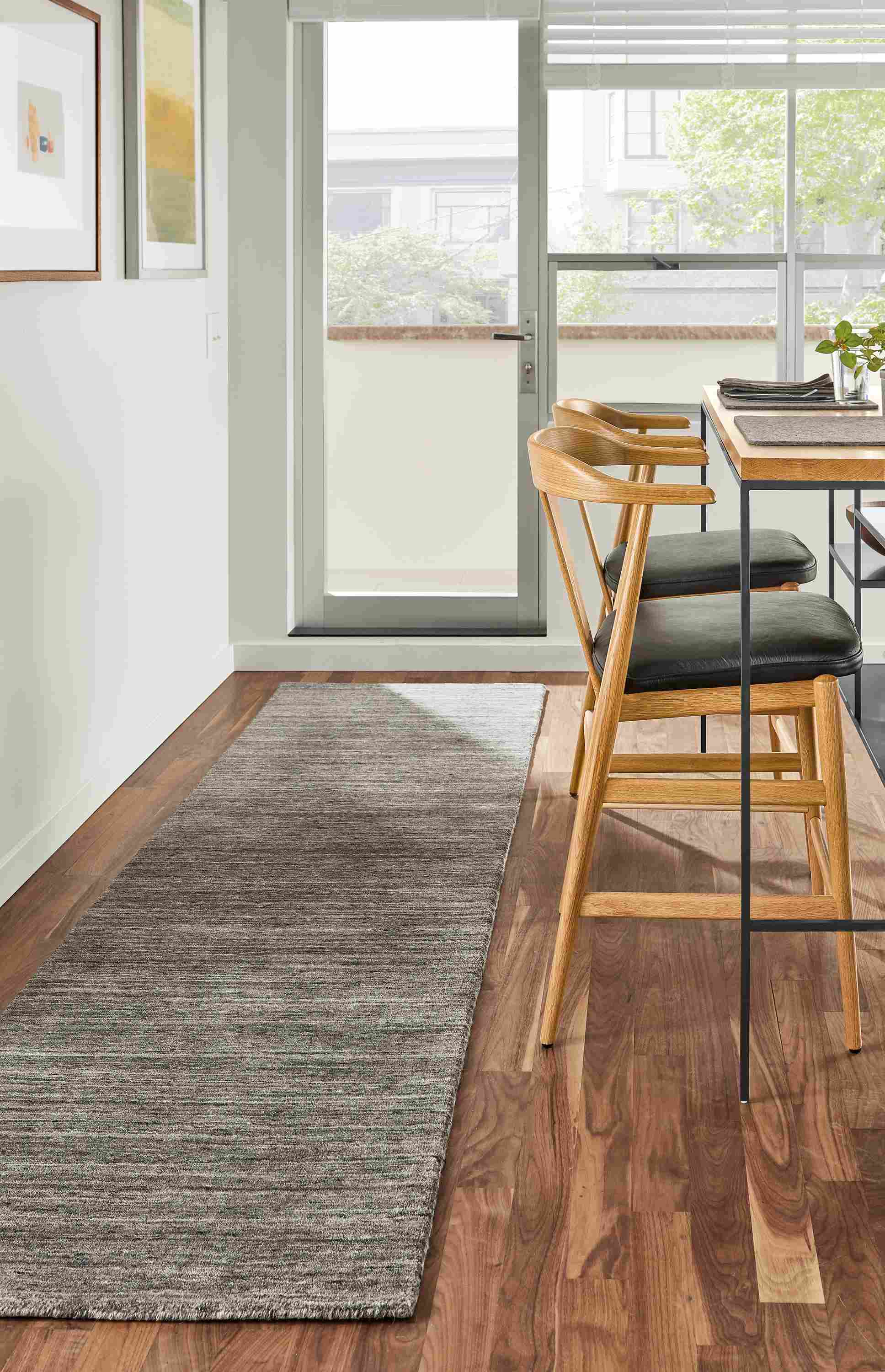 Kitchen room setting with two Evan counter stools in Pistel Leather and a Bowen Counter Table and a Nomad rug in Charcoal.