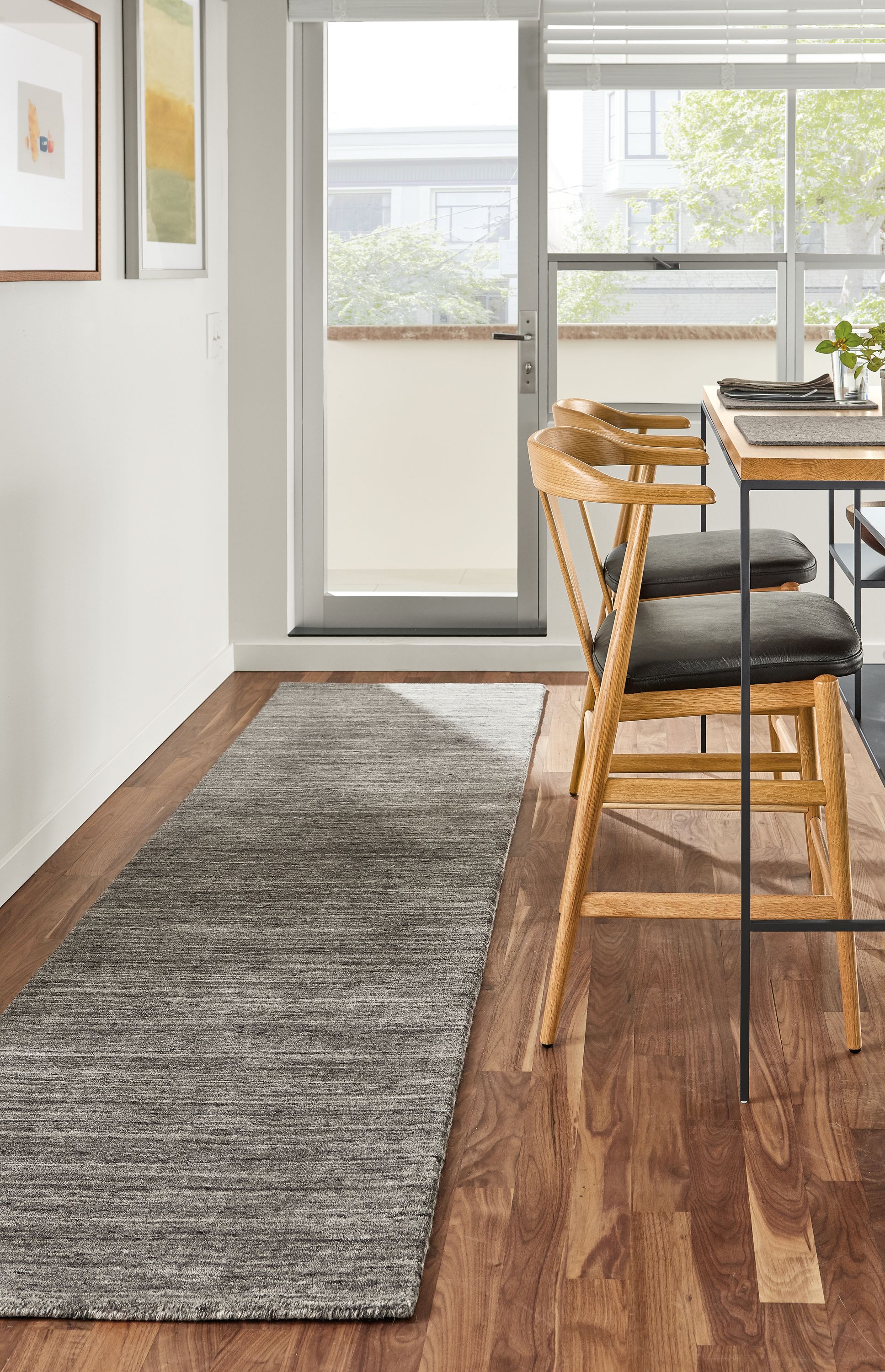 Kitchen room setting with two Evan counter stools in Pistel Leather and a Bowen Counter Table and a Nomad rug in Charcoal.