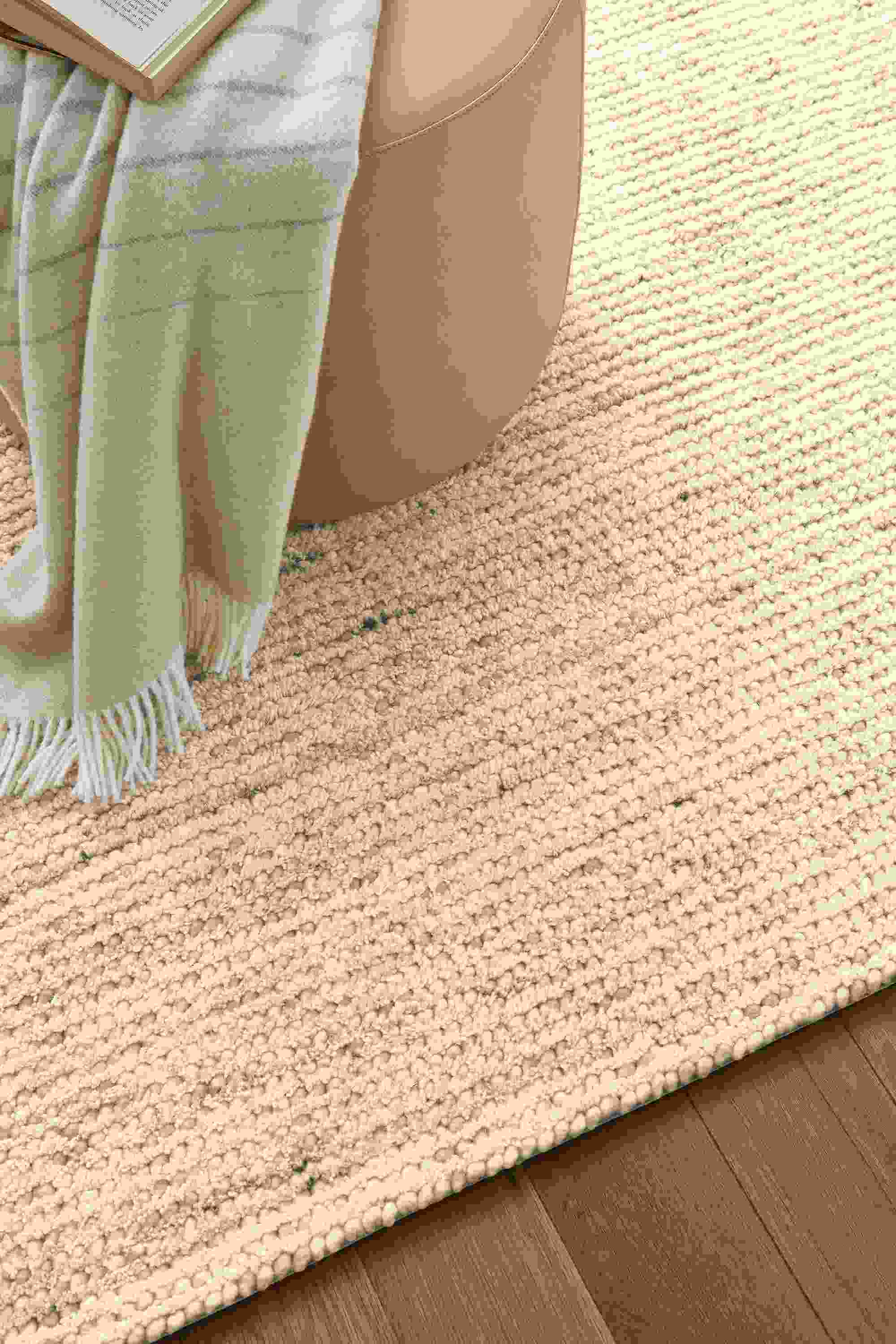 Living room with detail of Norfolk 8 by 10 rug in taupe and Lind round ottoman in Fiero Camel.