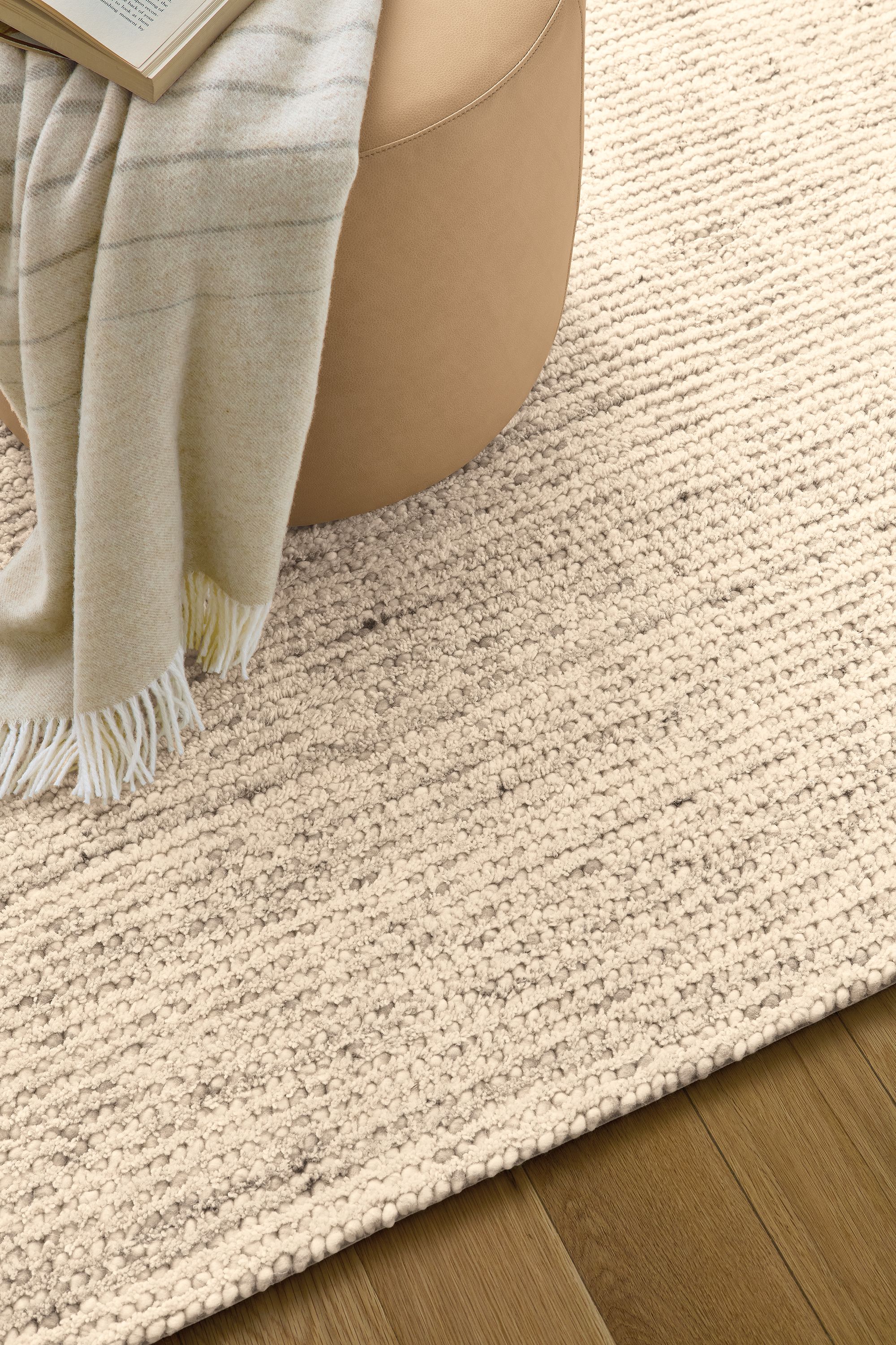 Living room with detail of Norfolk 8 by 10 rug in taupe and Lind round ottoman in Fiero Camel.