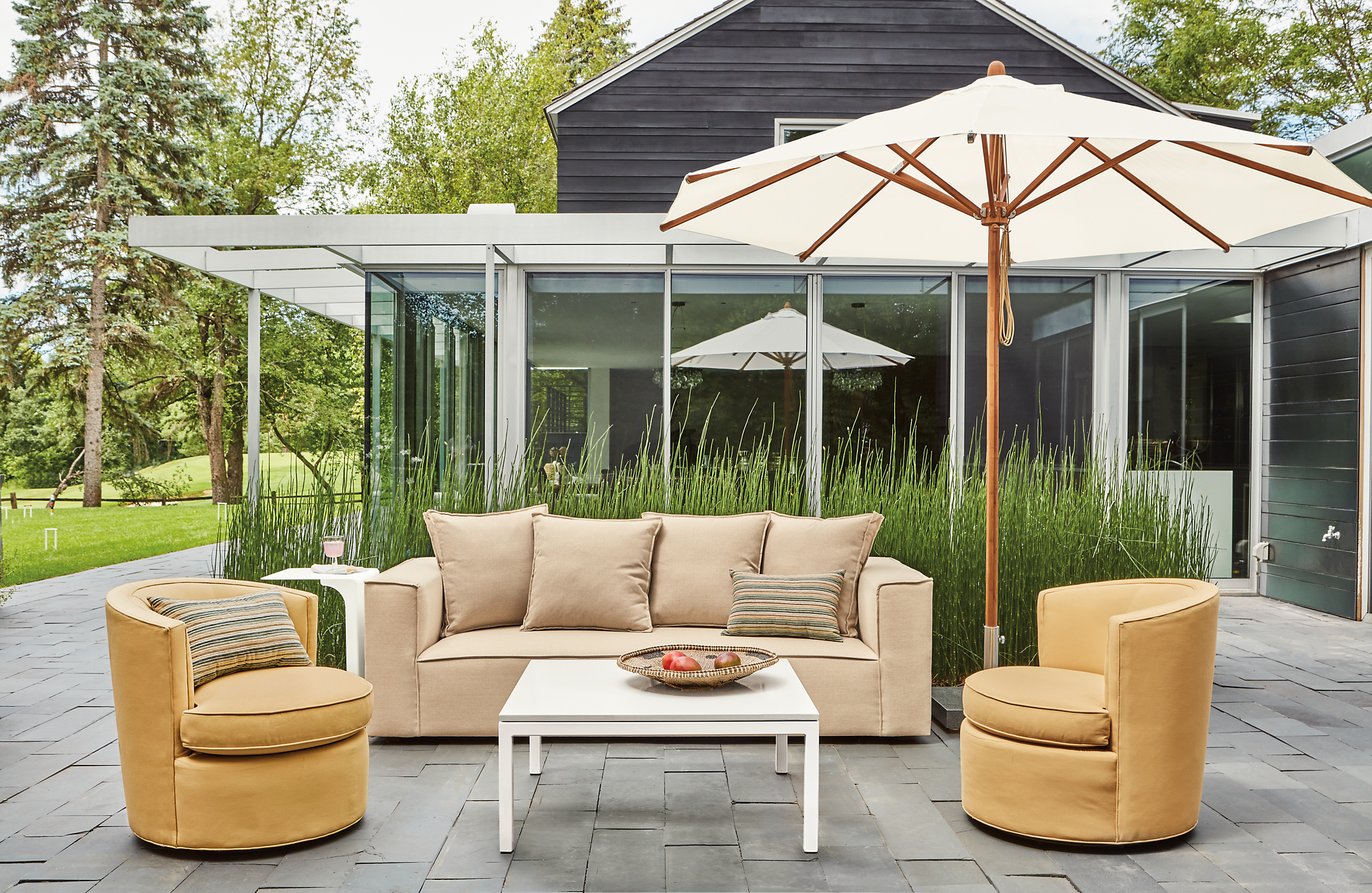 Outdoor patio setting with an Oasis sofa and Ambrose swivel chairs with a Cirro Umbrella and a Pratt coffee table in White.