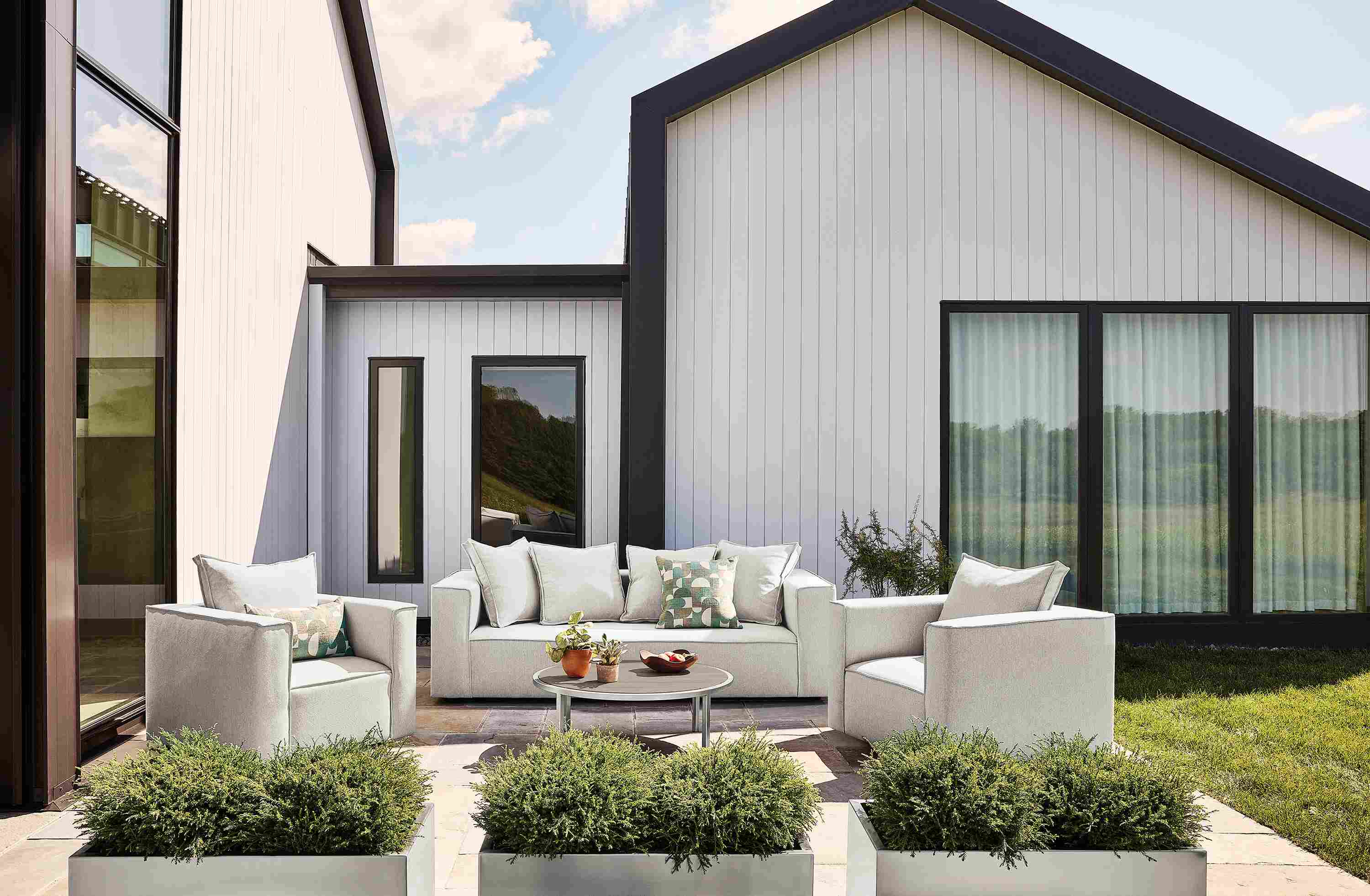 Patio with oasis sofa, 2 oasis swivel chairs and 2 oasis square ottomans all in mist grey fabric and Montego table in aged thermally modified oak.